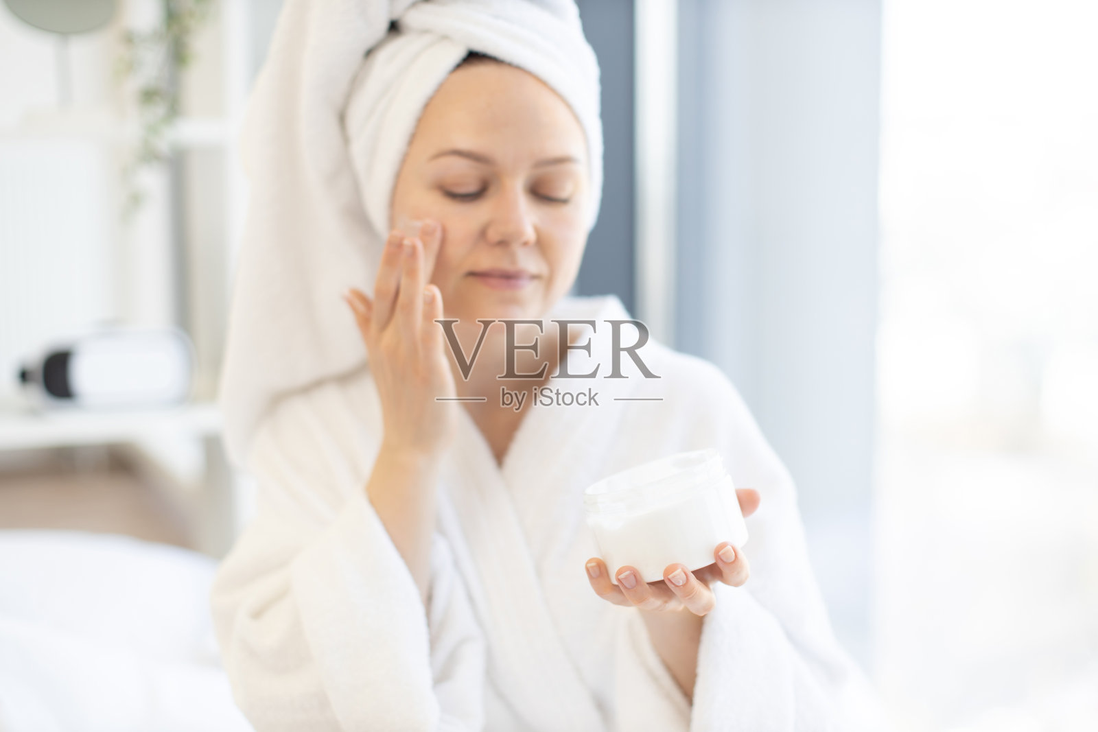 妇女在家里的卧室里从罐子里取出面霜照片摄影图片