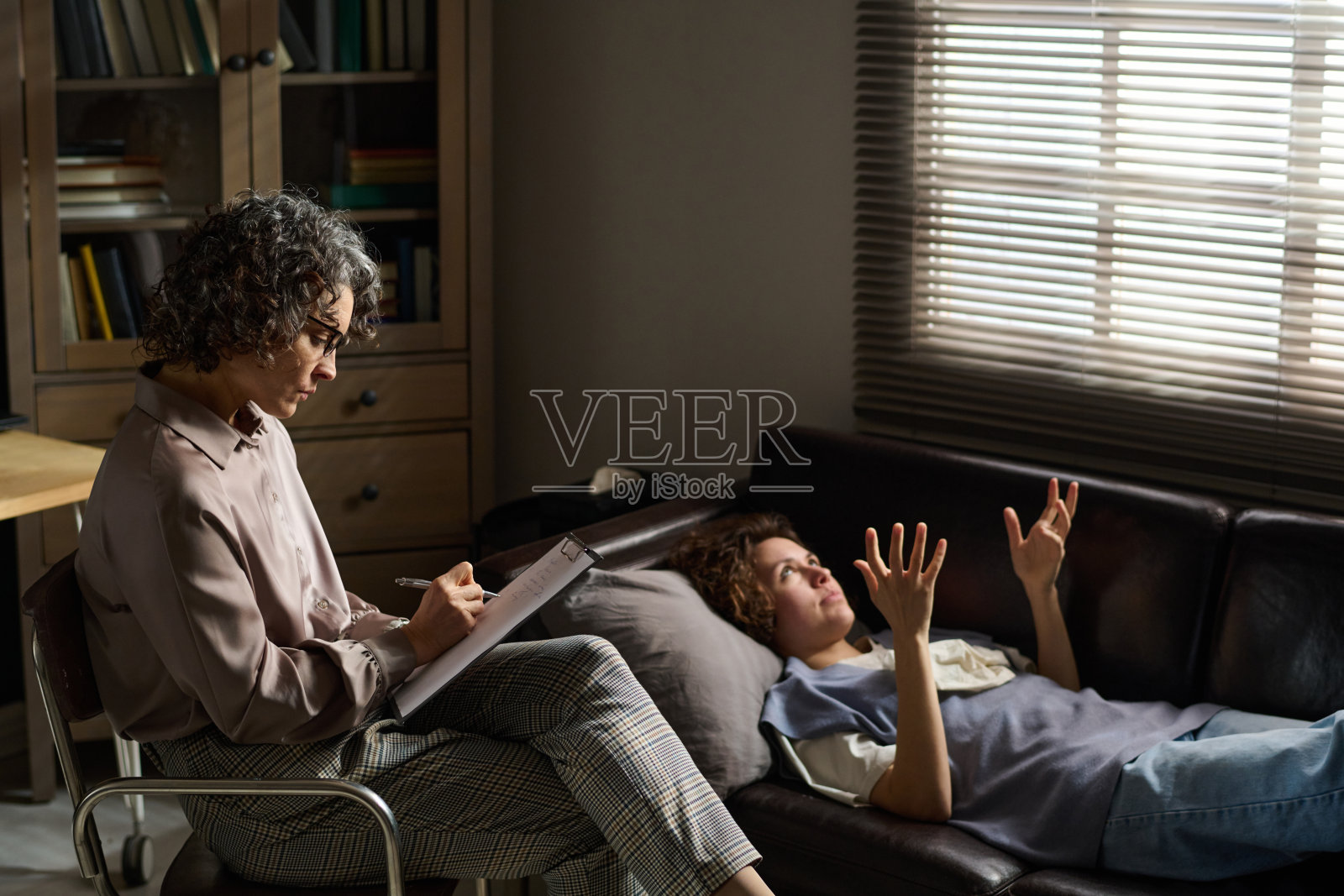 成熟的女性心理学家一边听病人说话，一边在文件中做笔记照片摄影图片