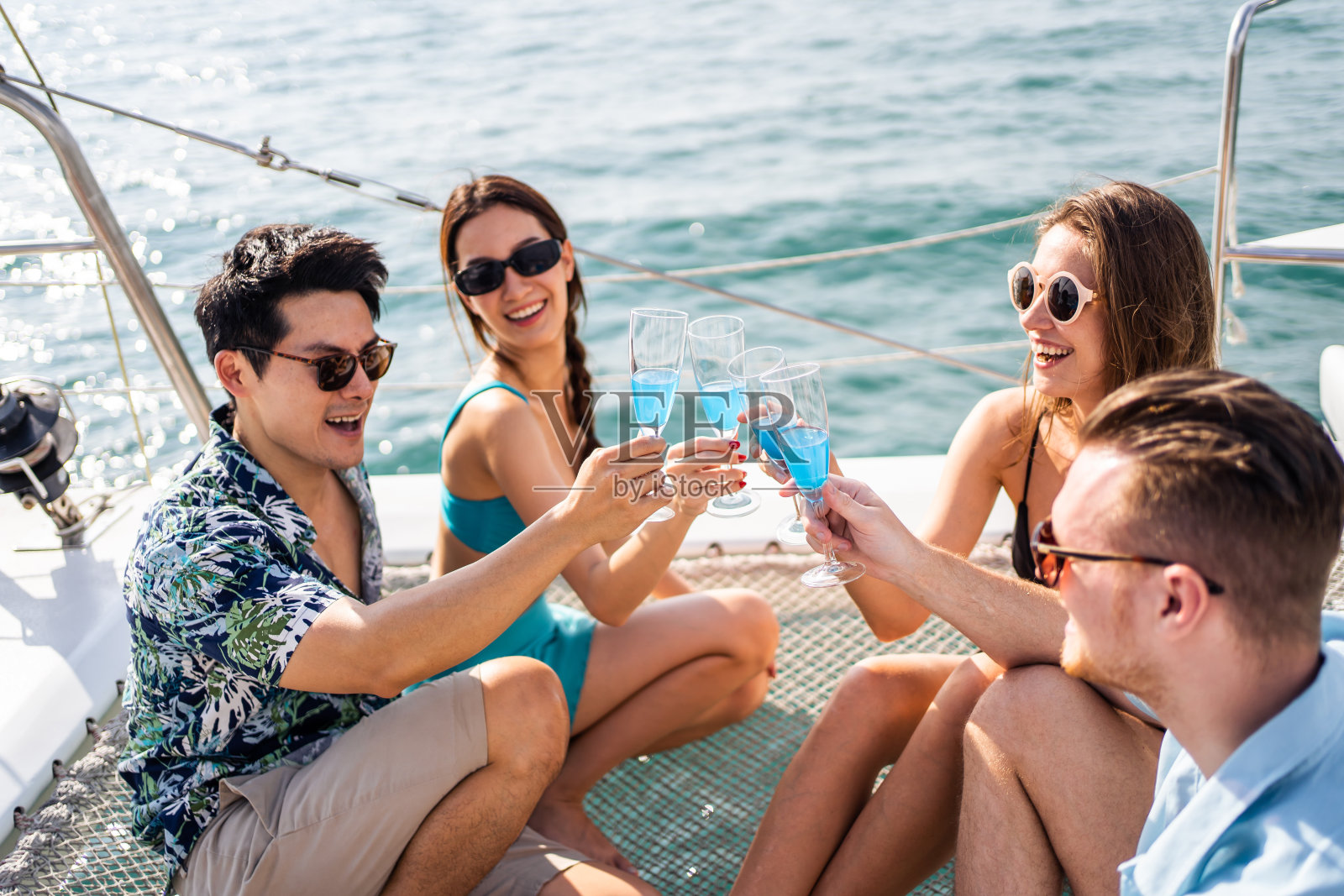 一群不同的朋友在游艇上开派对，喝着香槟。迷人的年轻男女聚在一起，庆祝节日，双体船在夏日夕阳下航行。照片摄影图片