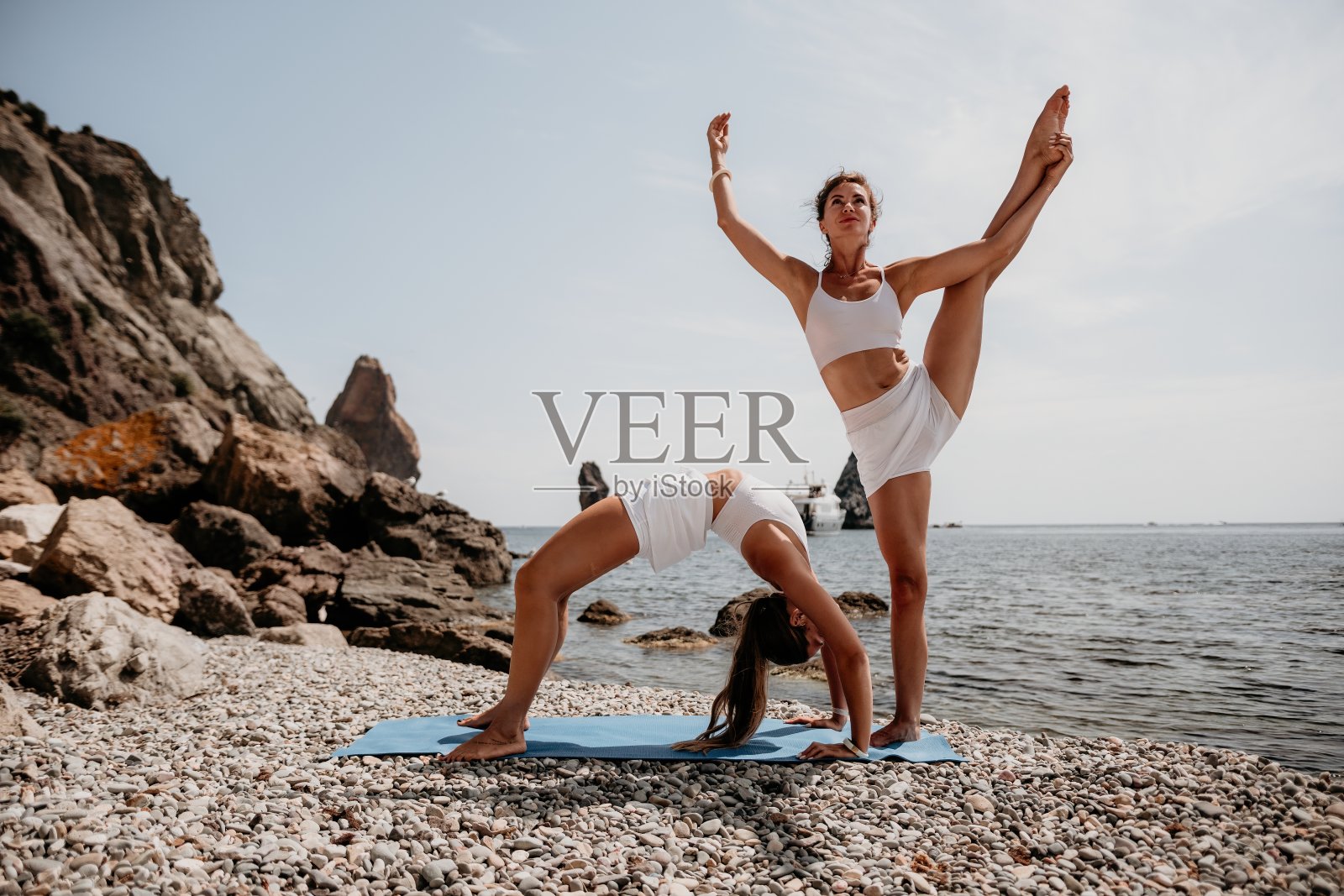 女子海上瑜伽。两个快乐的女人在海滩、海洋和岩石山上做瑜伽冥想。激励和鼓舞人心的健康和锻炼。户外自然健康生活方式，健身理念。照片摄影图片