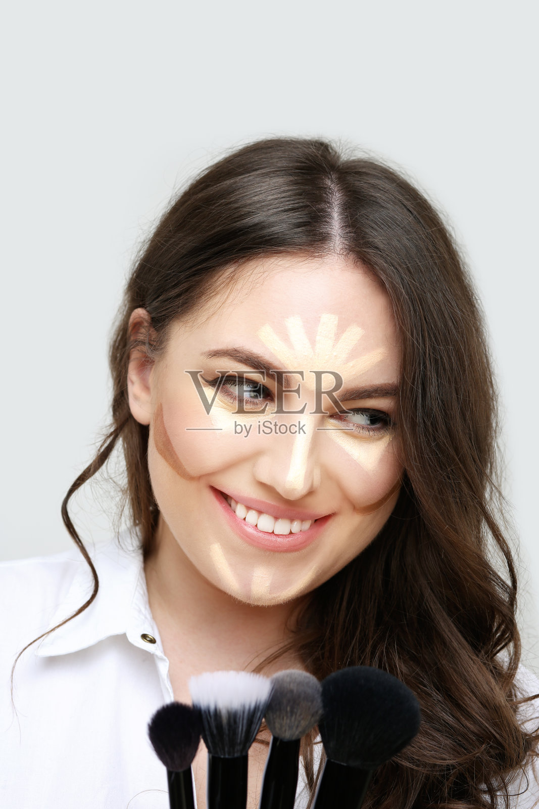 化妆。轮廓和突出化妆。用化妆刷化妆的女人。化妆粉和粉底的阴影在白色的背景照片摄影图片