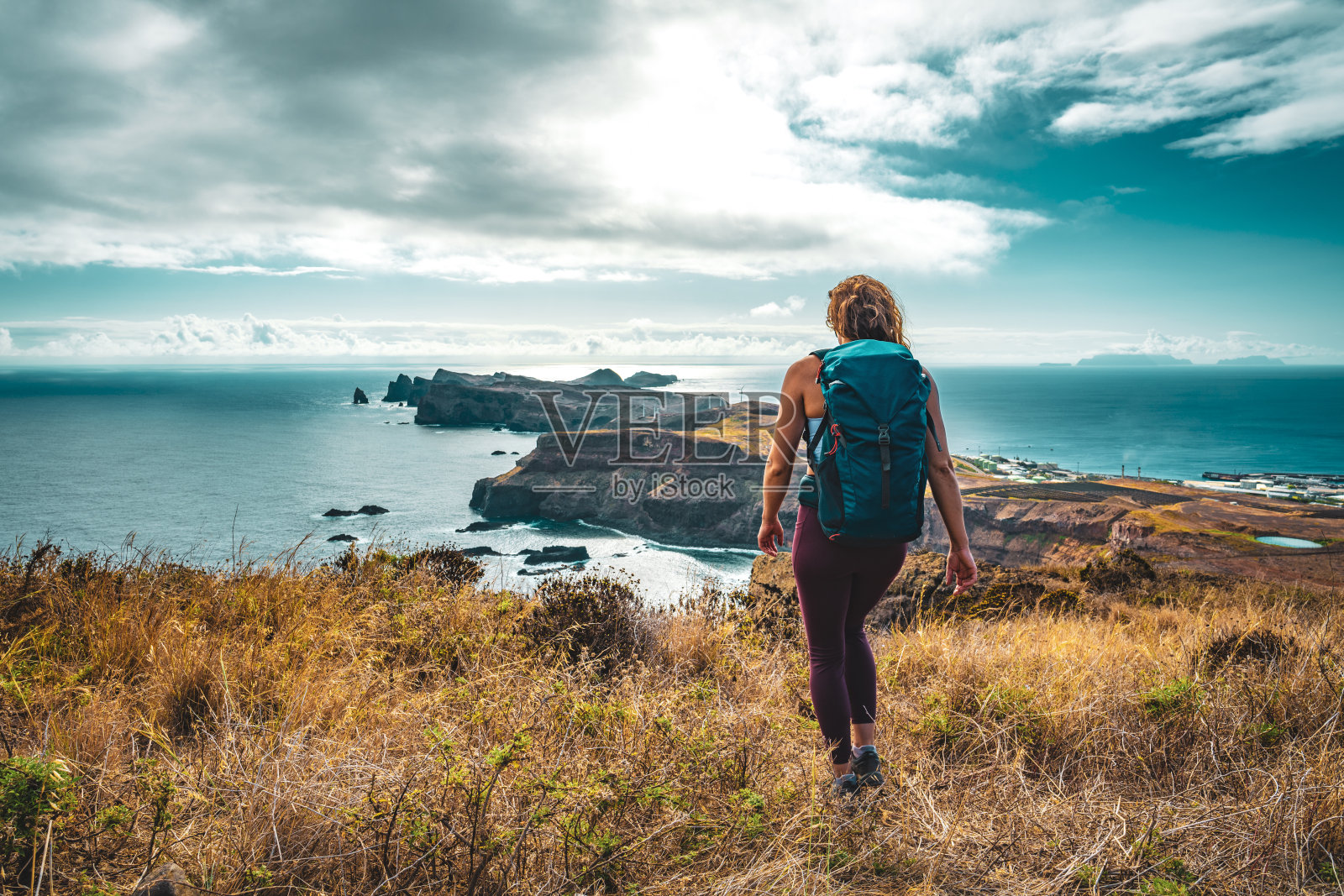 一名背包客女子喜欢在早晨沿着陡峭的悬崖徒步旅行，俯瞰大海和马德拉海岸崎岖的山麓。Ponta do Bode，马德拉岛，葡萄牙，欧洲。照片摄影图片