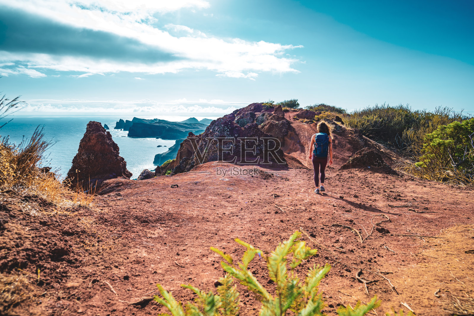 一名背包客女子喜欢在早晨沿着陡峭的悬崖徒步旅行，俯瞰大海和马德拉海岸崎岖的山麓。Ponta do Bode，马德拉岛，葡萄牙，欧洲。照片摄影图片