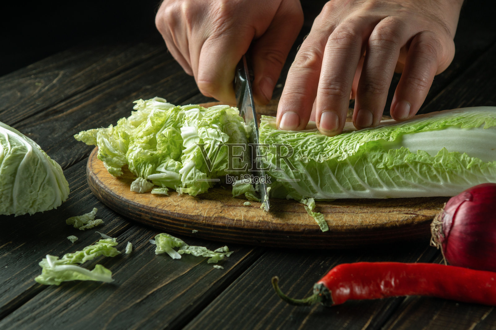 厨师用刀在菜板上切绿叶生菜的特写。深色背景下的美味早餐概念照片摄影图片