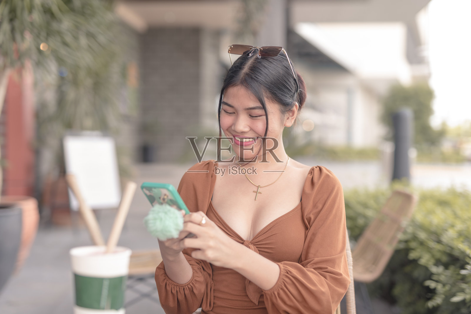 一位面带微笑的东南亚女性坐在咖啡馆外用手机给男友发信息。照片摄影图片