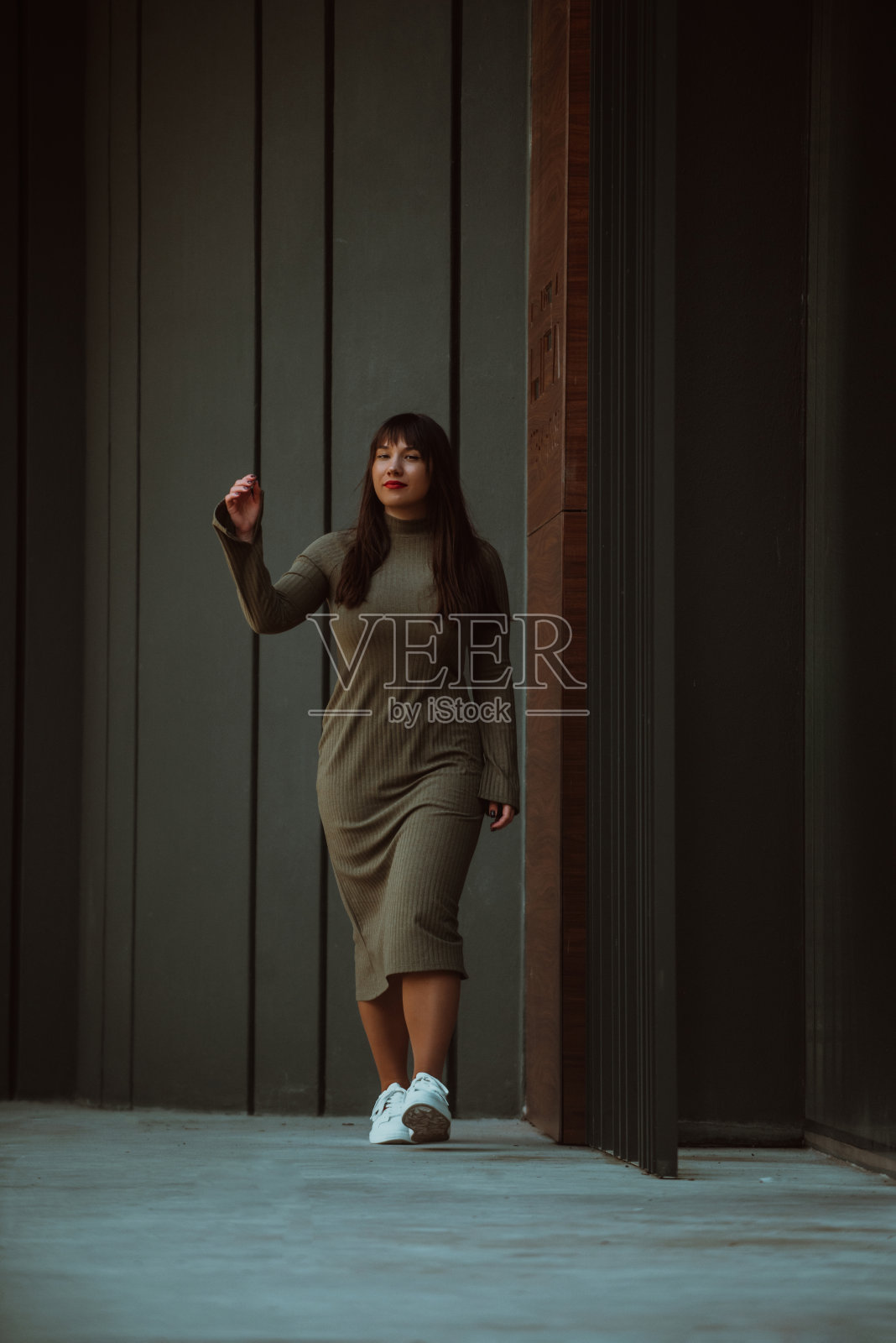 一个自信而时尚的大码女人穿着橄榄绿的连衣裙走过一座现代建筑，散发着美丽，赋权和自爱。照片摄影图片