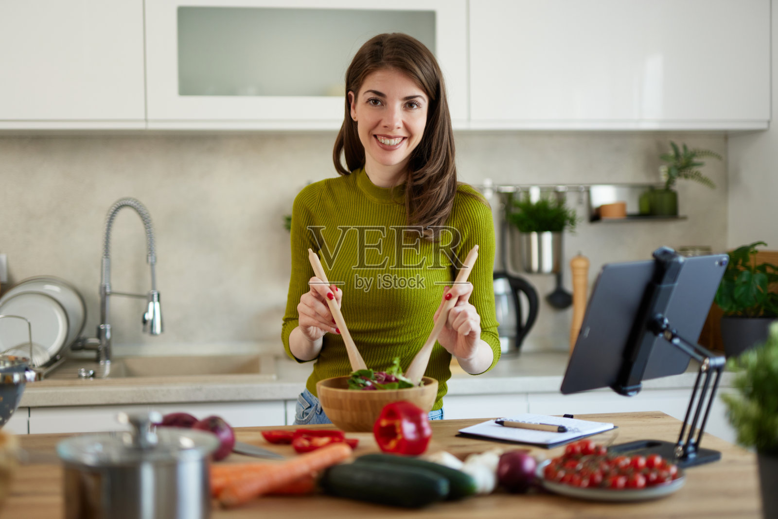 年轻女子站在厨房用网上食谱做沙拉照片摄影图片