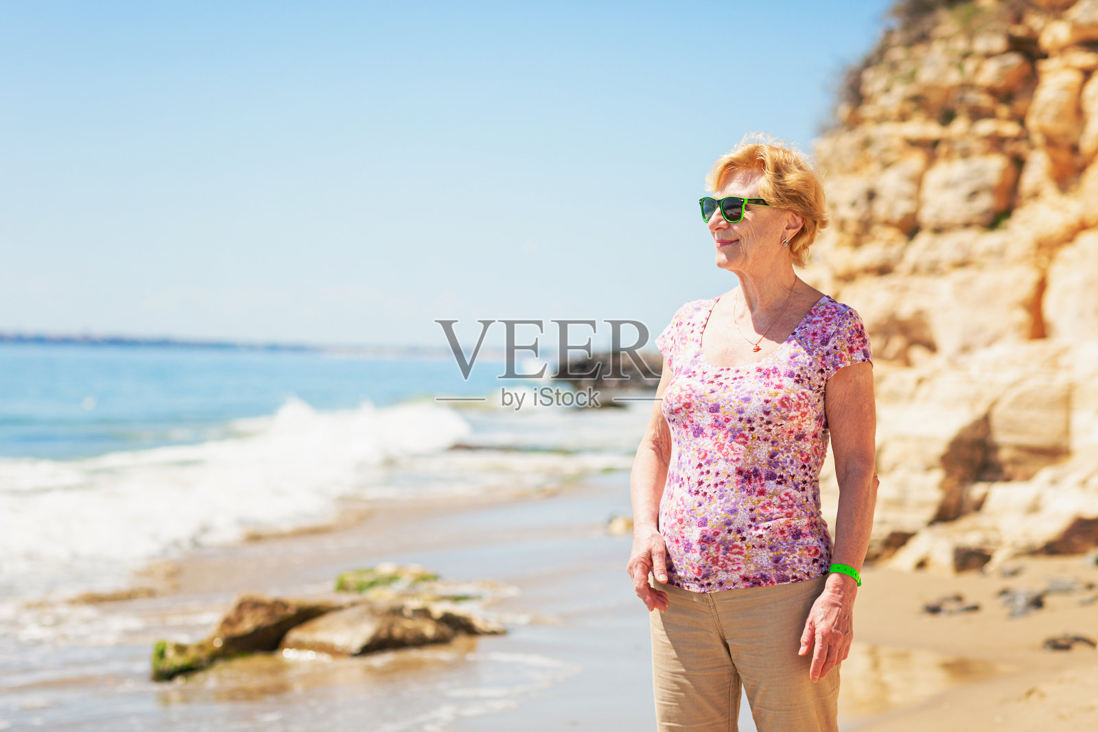 一位戴着墨镜的老妇人站在沙滩上看着大海照片摄影图片