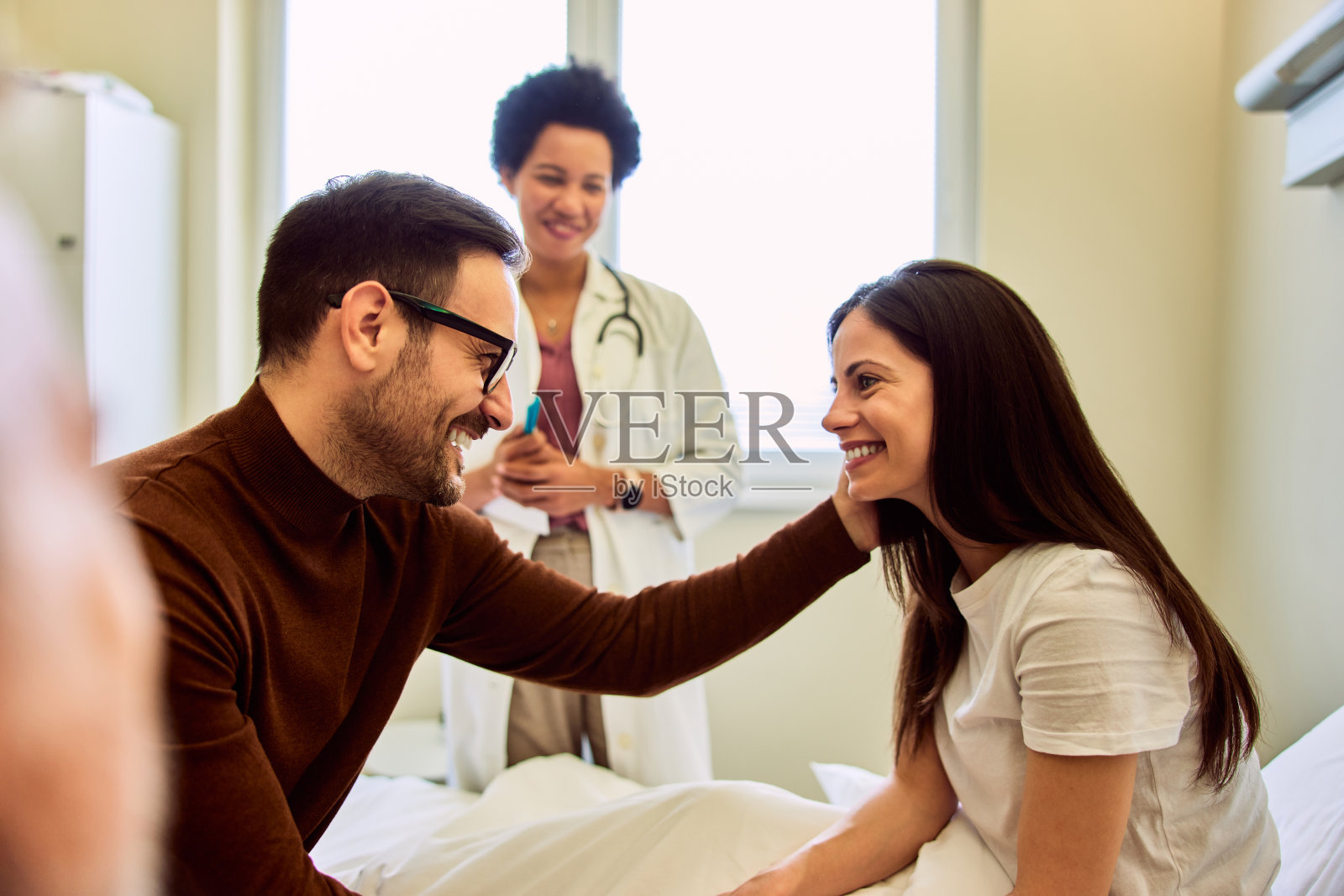 一位丈夫到医院看望妻子，旁边站着一位女医生。照片摄影图片