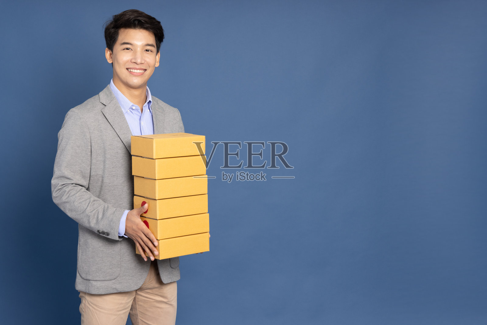 亚洲商人手持包裹，包裹盒隔离在蓝色背景上，传递快递和航运服务理念照片摄影图片
