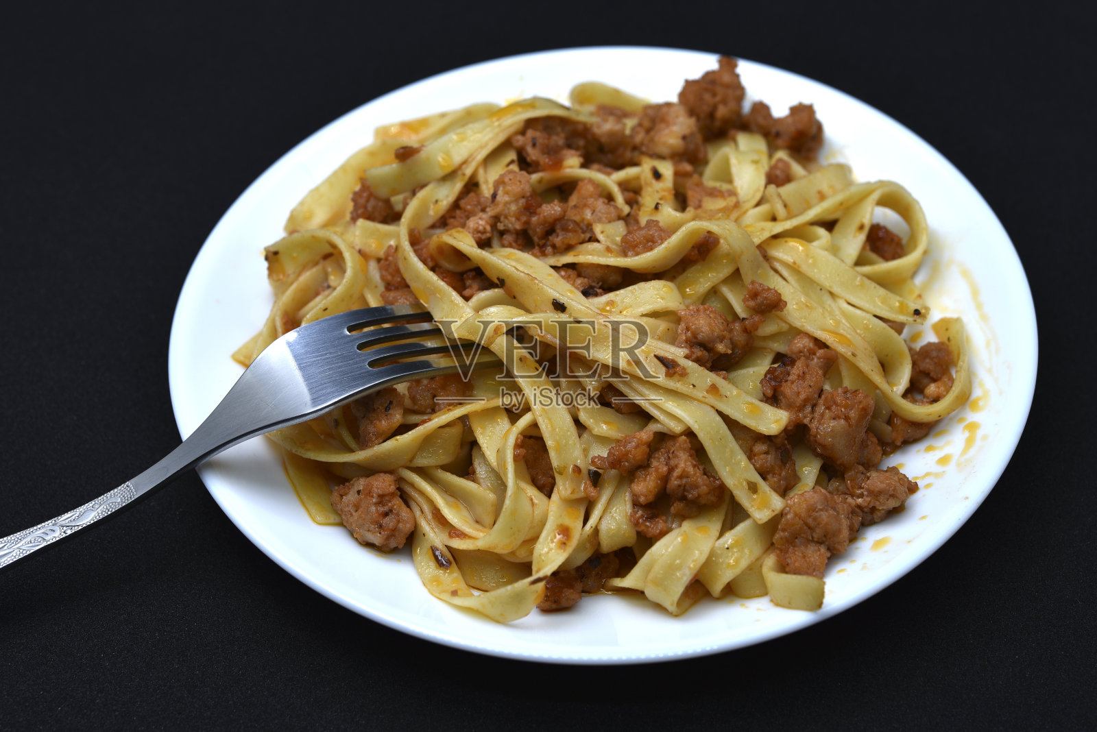 用叉子盛在白色盘子里的意大利面食。一盘黑底肉粉。照片摄影图片