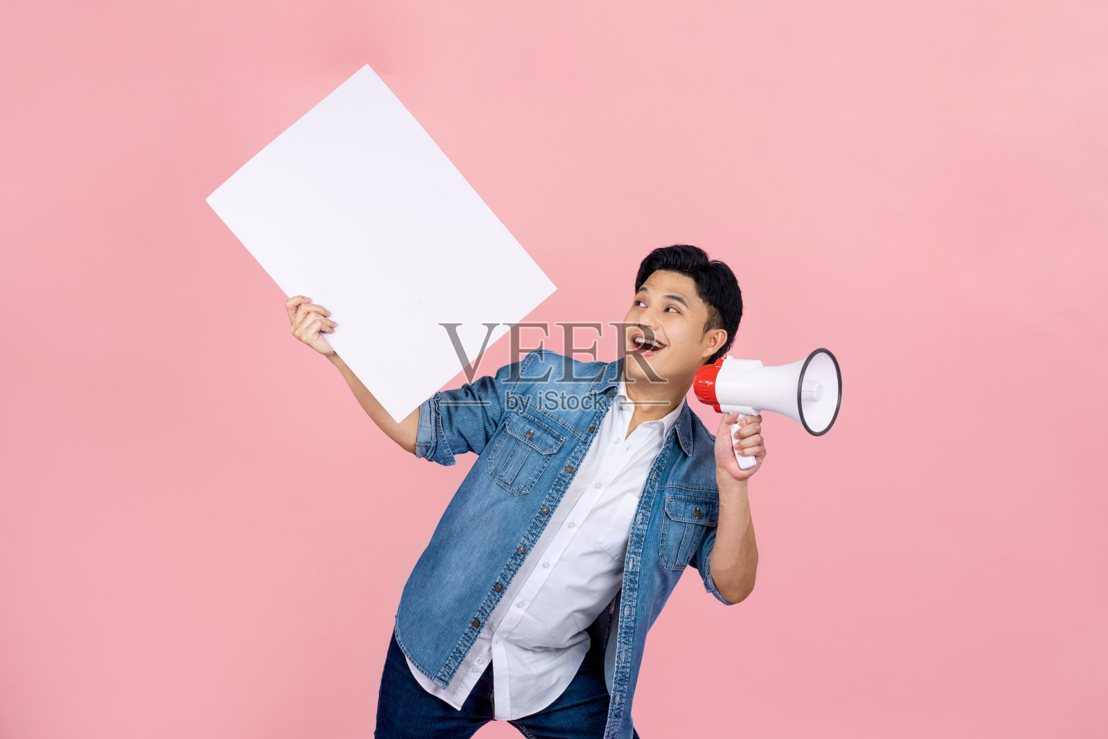 微笑快乐的亚洲人对着扩音器喊着公告，拿着粉红色背景上空白的演讲泡泡。照片摄影图片