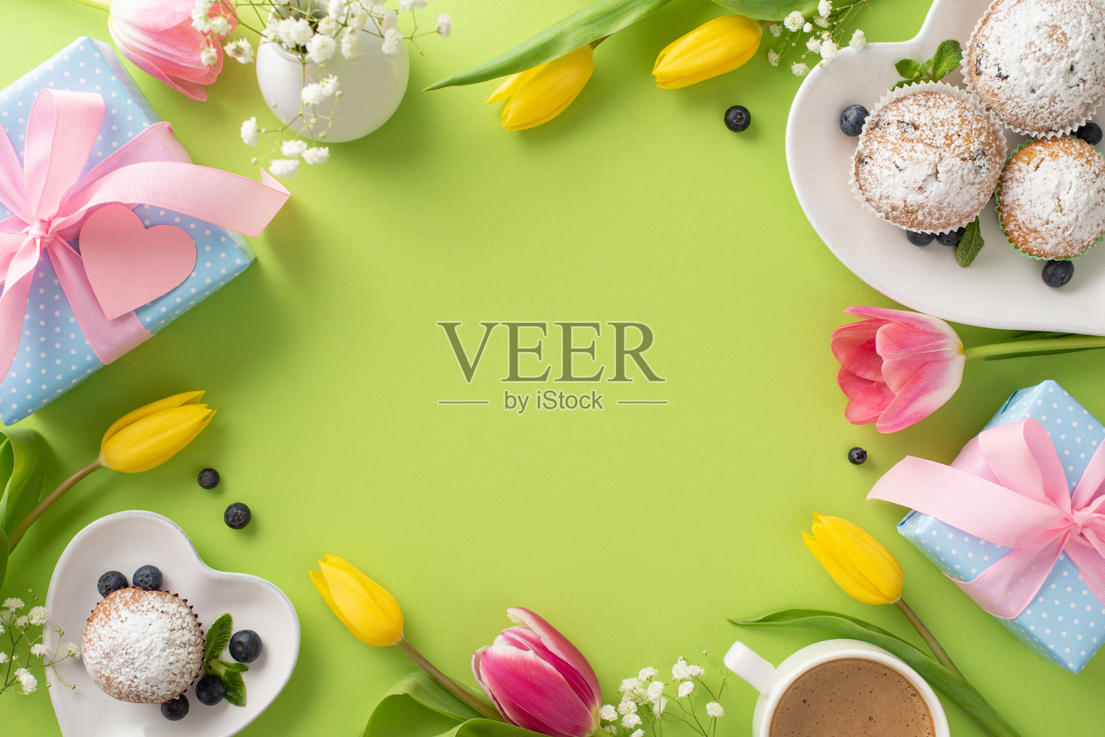 母亲节快乐，时尚的餐桌上有美味的纸杯蛋糕、礼物、咖啡杯和郁金香，在柔和的绿色背景上排列在顶部，空白的空间用来问候照片摄影图片