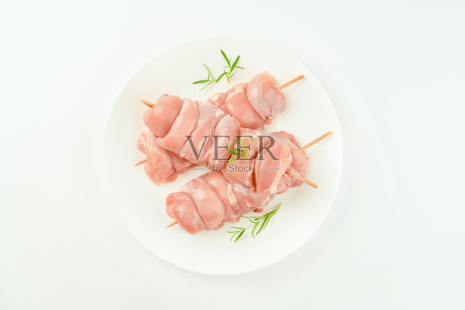把去皮的生鸡腿肉串在白色盘子里，配上新鲜的迷迭香，在白色背景上卖给超市。零售食品。鸡肉串。鸡肉。设计师采购。照片摄影图片