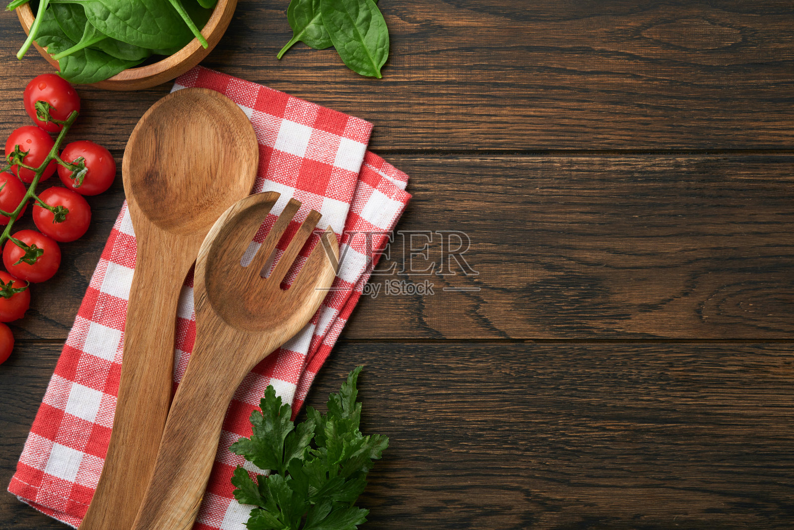 砧板上有厨房用的勺子，红色的餐巾和欧芹，在旧木制的深色背景上做饭用的西红柿。素食，健康还是烹饪的概念。食物背景与文字的自由空间。照片摄影图片