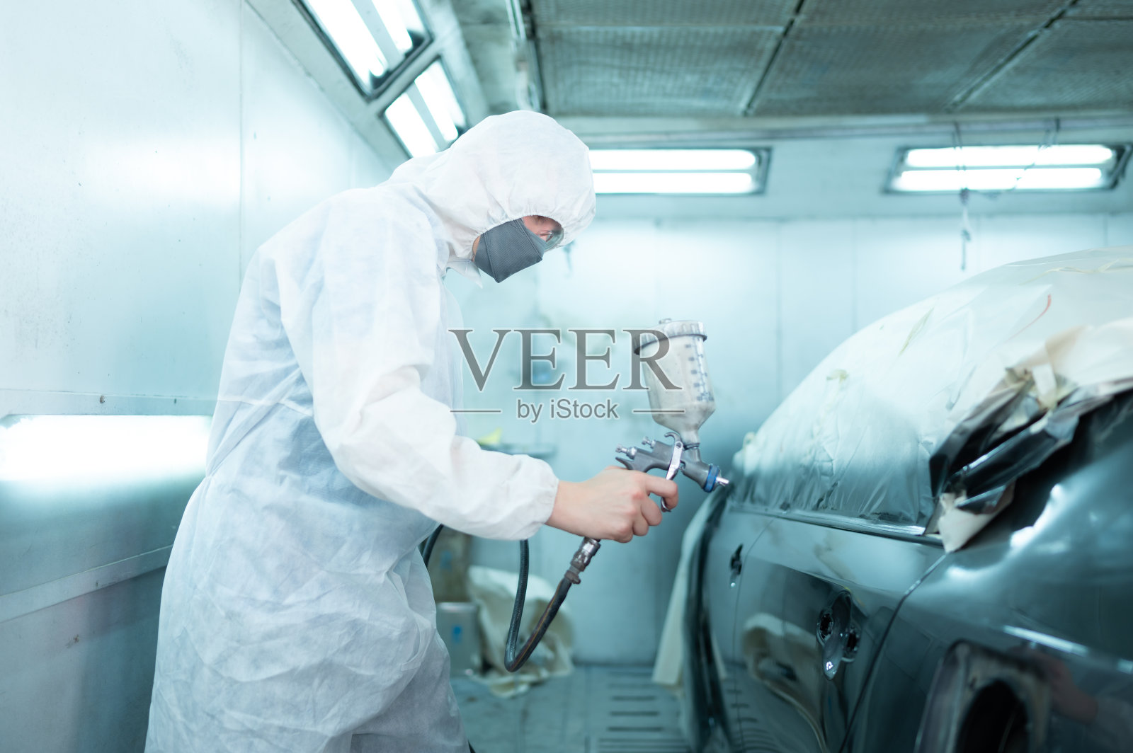 汽车喷漆室汽修工用喷嘴向车身侧面精心喷涂，营造出与汽车原有颜色相融合的美感。照片摄影图片