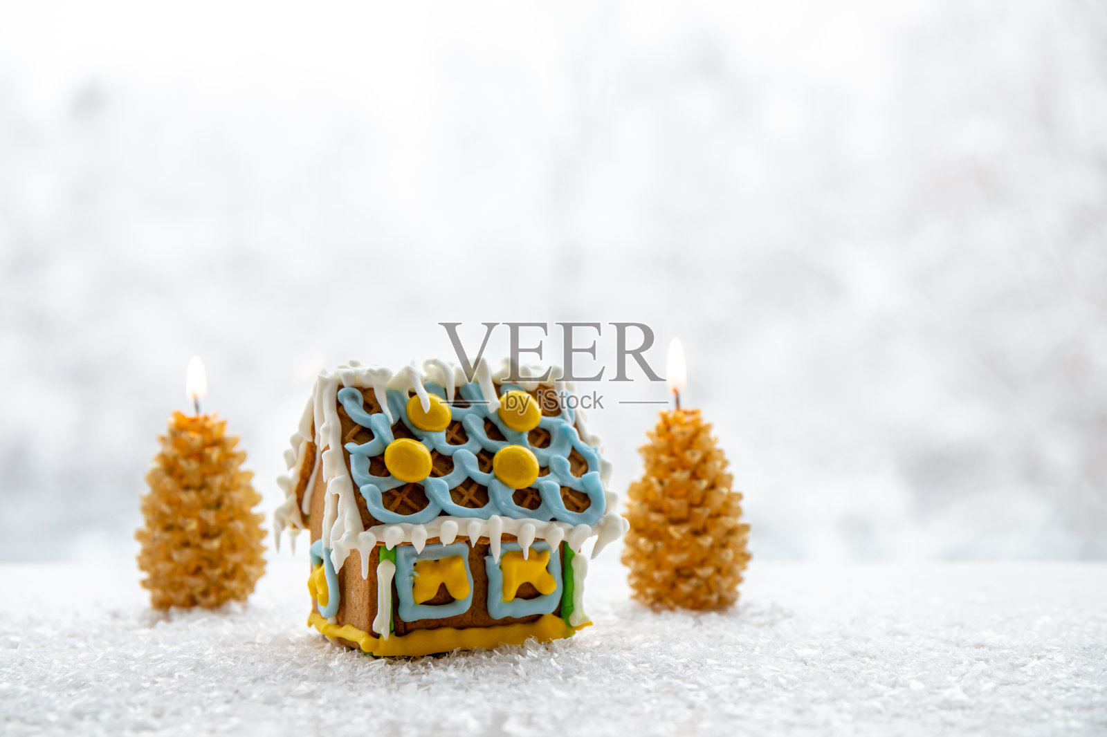 可爱的小姜饼屋，装饰着黄色和蓝色的糖霜，云杉树形状的蜡烛燃烧的背景与冬天的风景。大量的拷贝空间。照片摄影图片