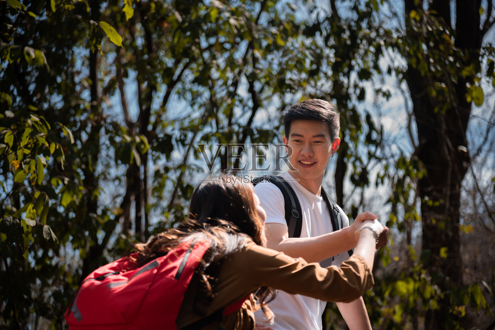 年轻的亚洲游客夫妇在岩石上攀岩，男人搀扶着女人徒步旅行，在户外欣赏美丽的大自然。伴侣或夫妇冒险旅行一起在森林夏天站在山顶。照片摄影图片