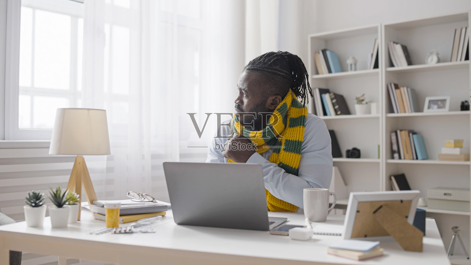 一个病人裹着围巾，喝着热茶，在笔记本电脑上打字，就像一个自由职业者照片摄影图片