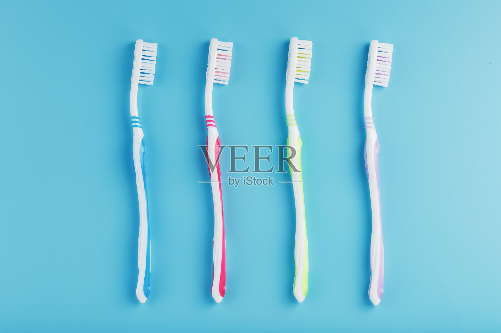 不同颜色的牙刷在蓝色背景上排成一排。照片摄影图片