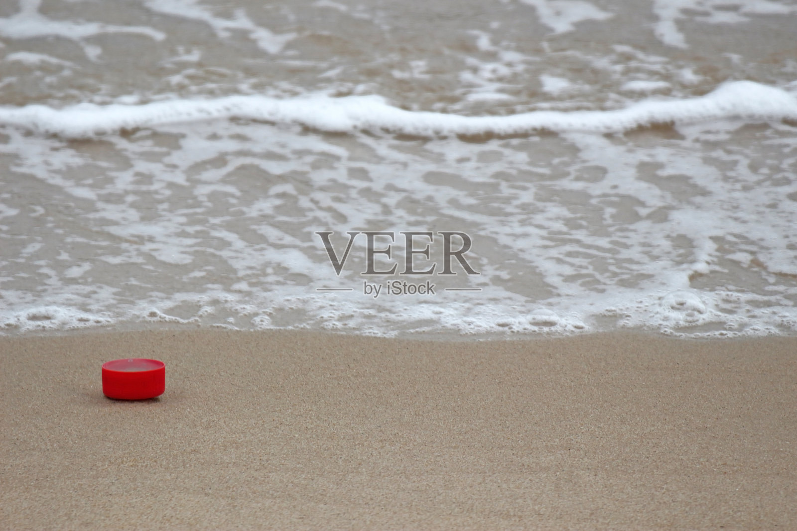 红色塑料瓶盖污染了干净的海滩照片摄影图片