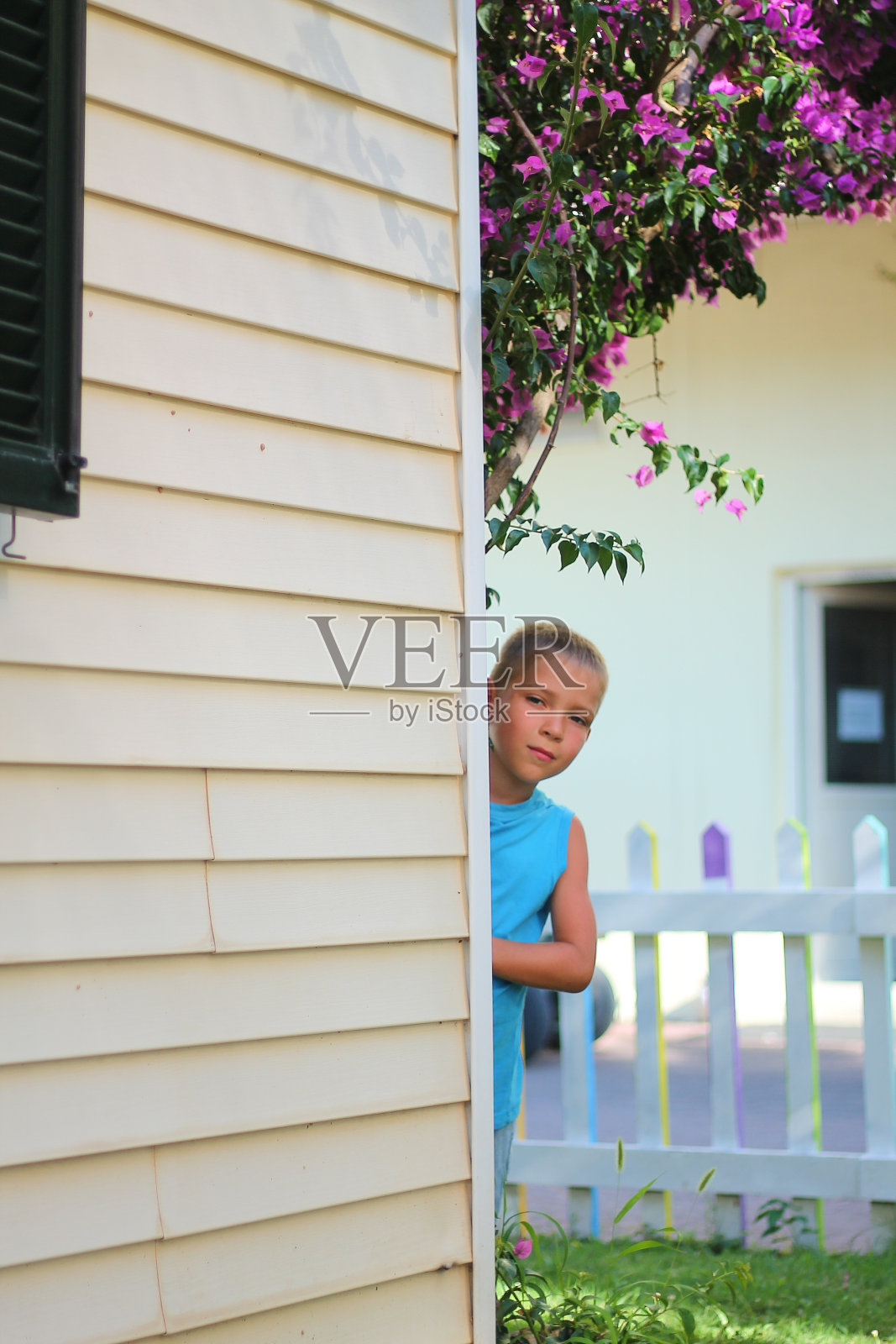 夏日花园中，一个可爱的蓝衣男孩从屋角向外张望照片摄影图片