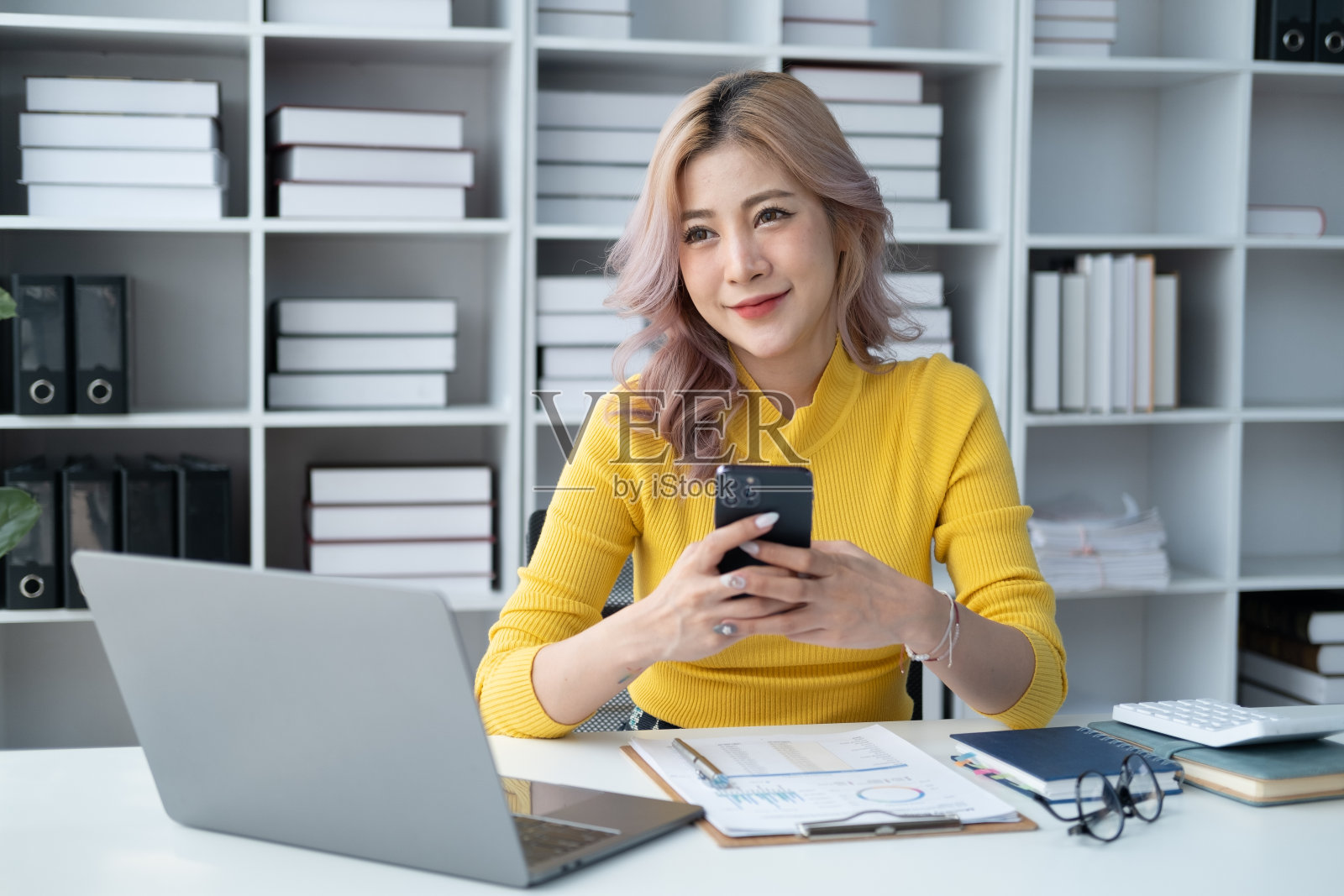 自信的年轻亚洲女商人坐在办公桌前使用智能手机，发短信或与朋友聊天。照片摄影图片