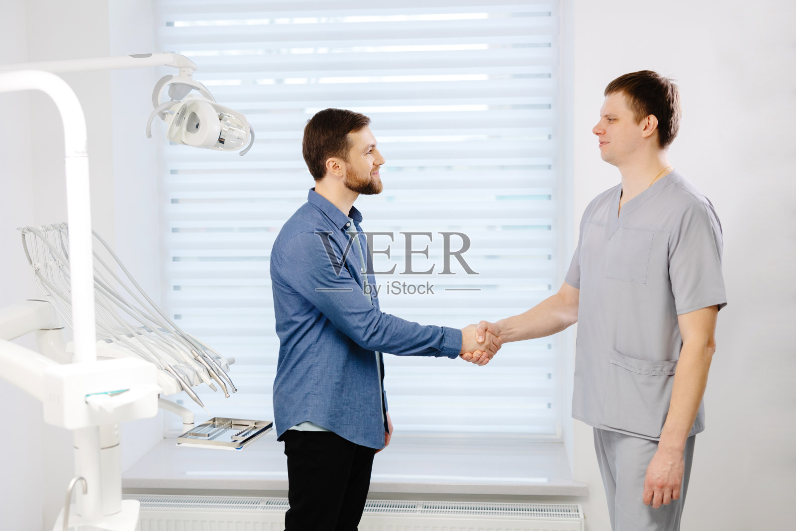 医生接见病人。一名男子站在办公室牙医椅旁与牙医握手。照片摄影图片
