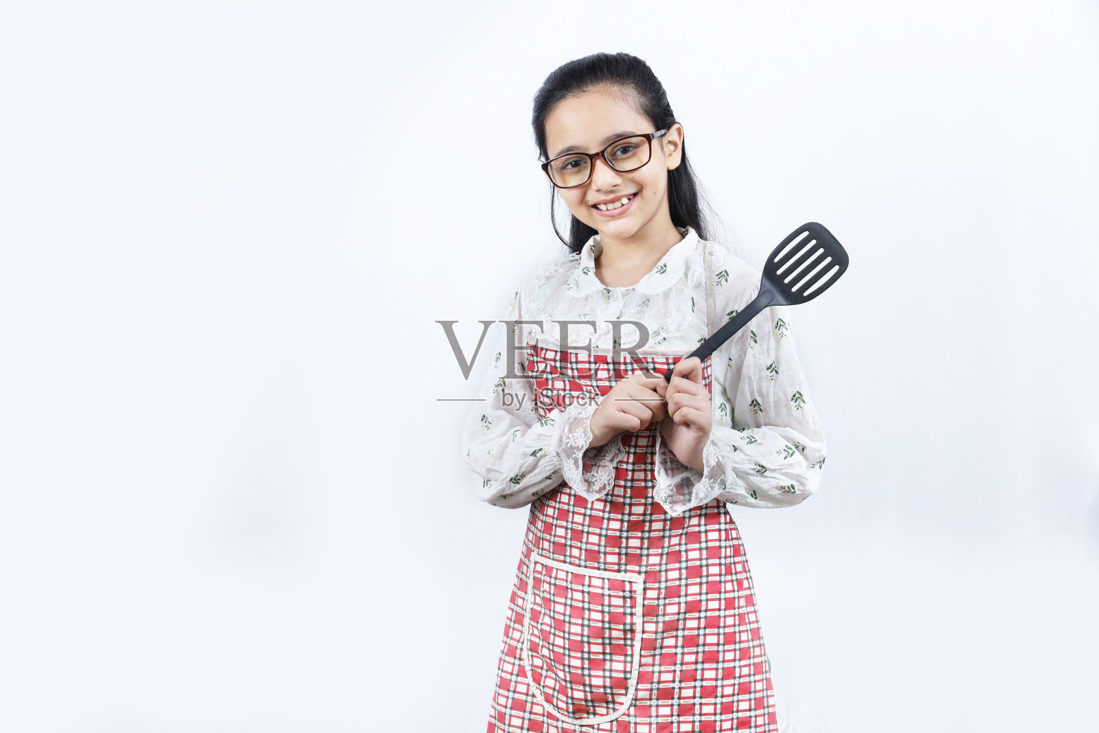 快乐的印度少女在厨房拿着烹饪用具的肖像。擀面杖，煎勺，长勺，煎锅。照片摄影图片