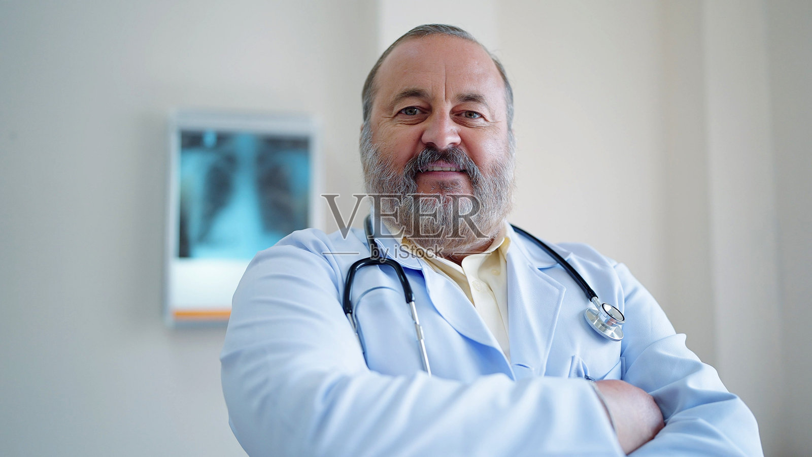 穿着白大褂，戴着听诊器的白人资深男医生的肖像，微笑着，双臂交叉站在医院里看着镜头照片摄影图片