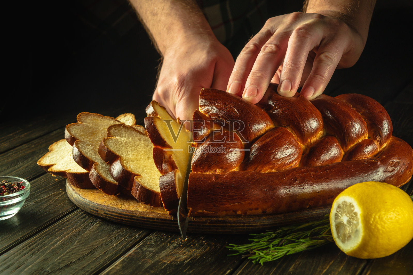 全麦面包放在厨房的木板上，厨师拿着刀切。餐桌上的新鲜面包特写。小麦kolach在厨房餐桌上的健康饮食和传统的烘焙理念照片摄影图片