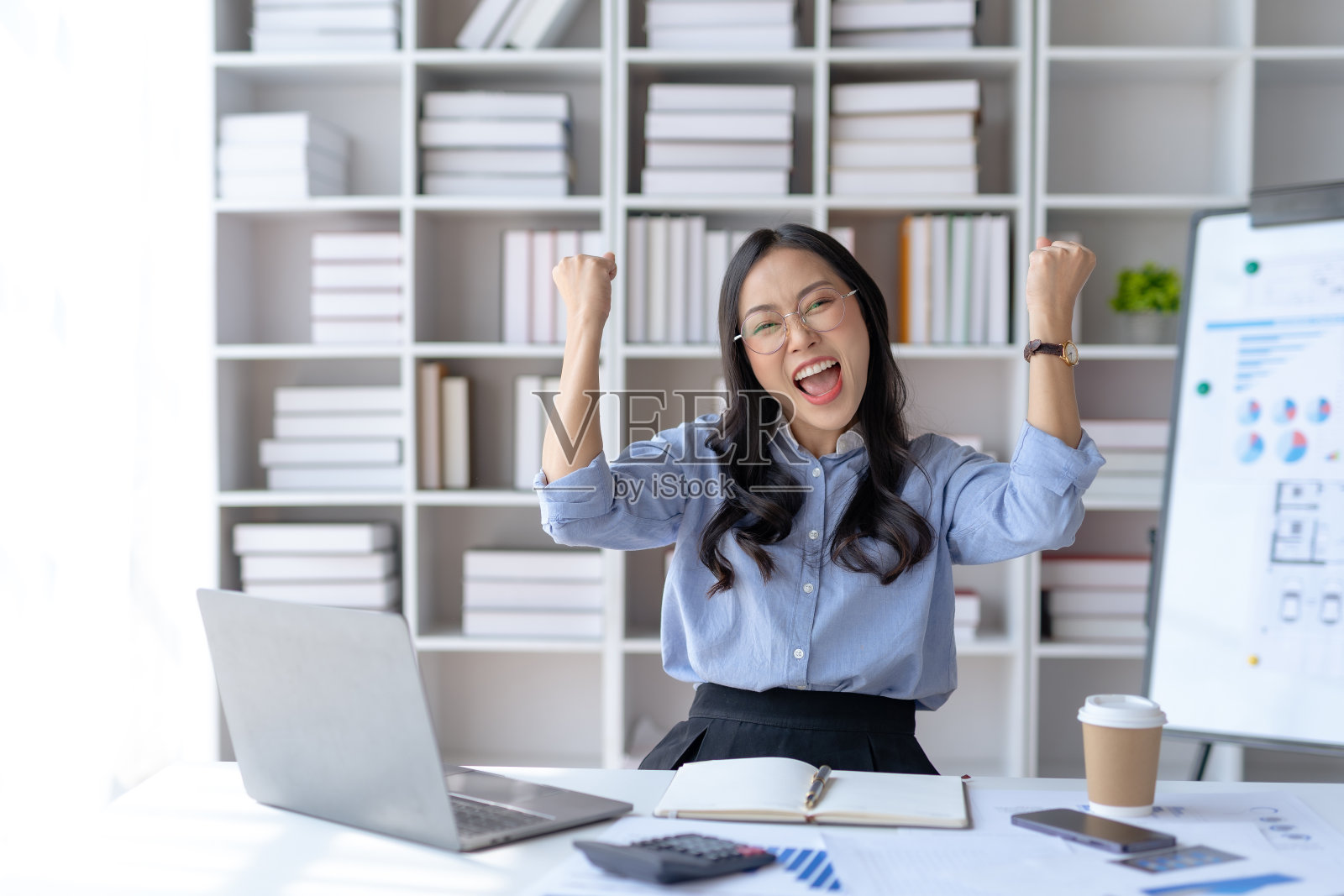 快乐的亚洲女商人举起胜利的手，在笔记本电脑上开心地微笑。工作中成功的概念。照片摄影图片
