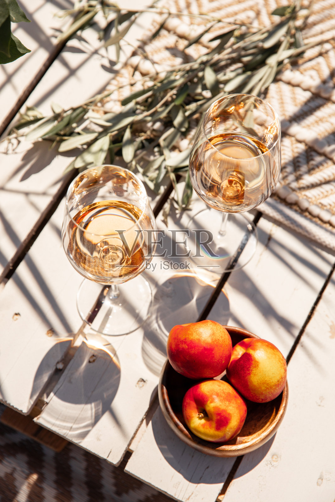 在地中海阳光明媚的日子里，在白色的木桌上喝着玫瑰色的酒杯，吃着桃子照片摄影图片