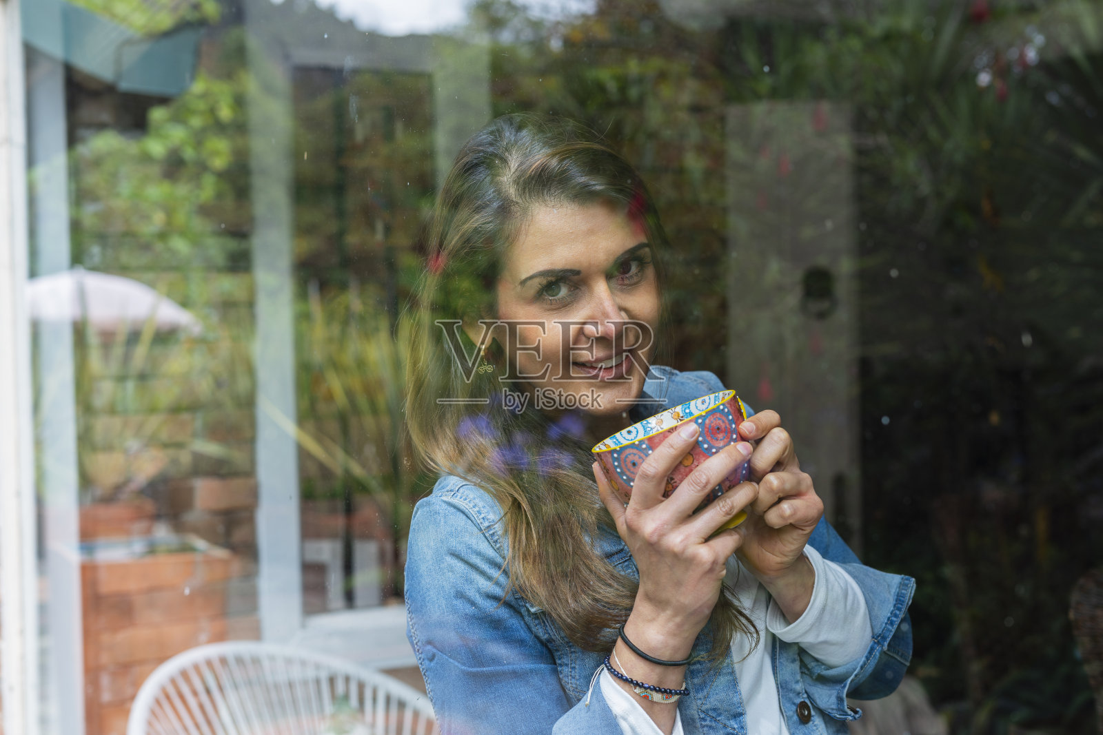 一位拉丁裔妇女站在她的情感治疗师办公室的窗前，享受着一杯咖啡照片摄影图片