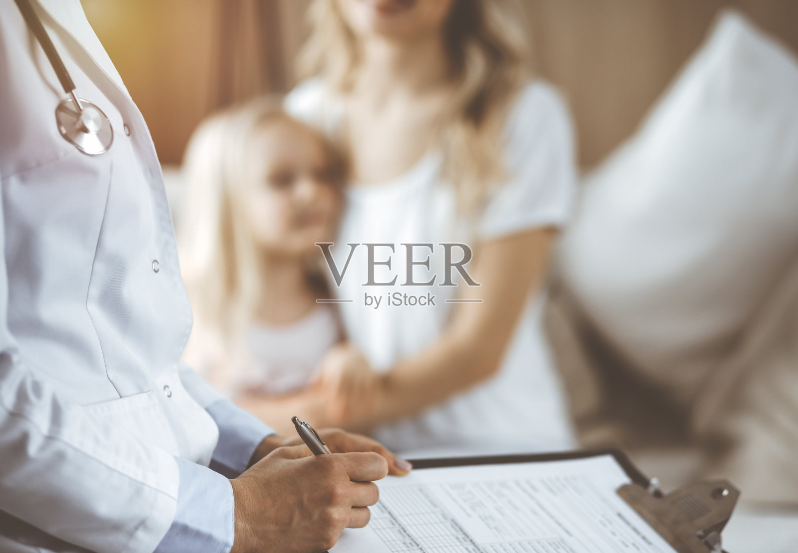 医生和病人。儿科医生在家里给小女孩和她妈妈做检查时使用了剪贴板。体检时可爱的白种人孩子快乐。医学的概念照片摄影图片