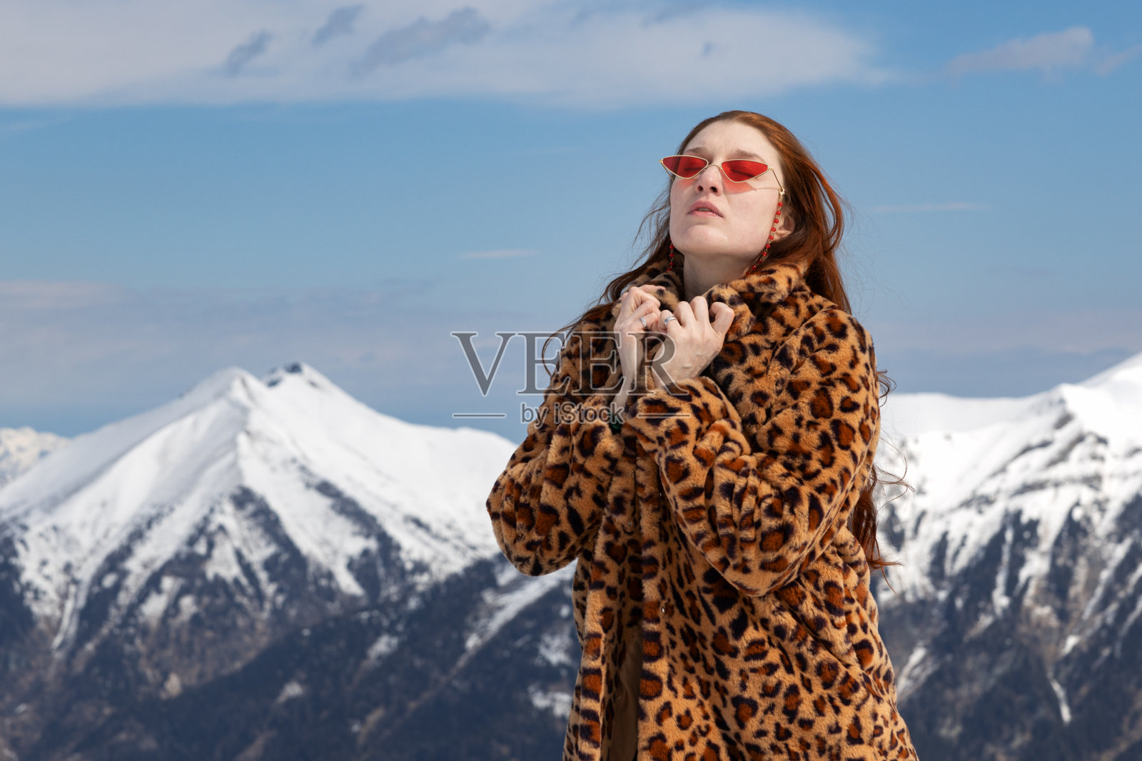 奥地利，一名模特穿着大衣，戴着明亮的眼镜，闭着眼睛站在群山的背景下照片摄影图片