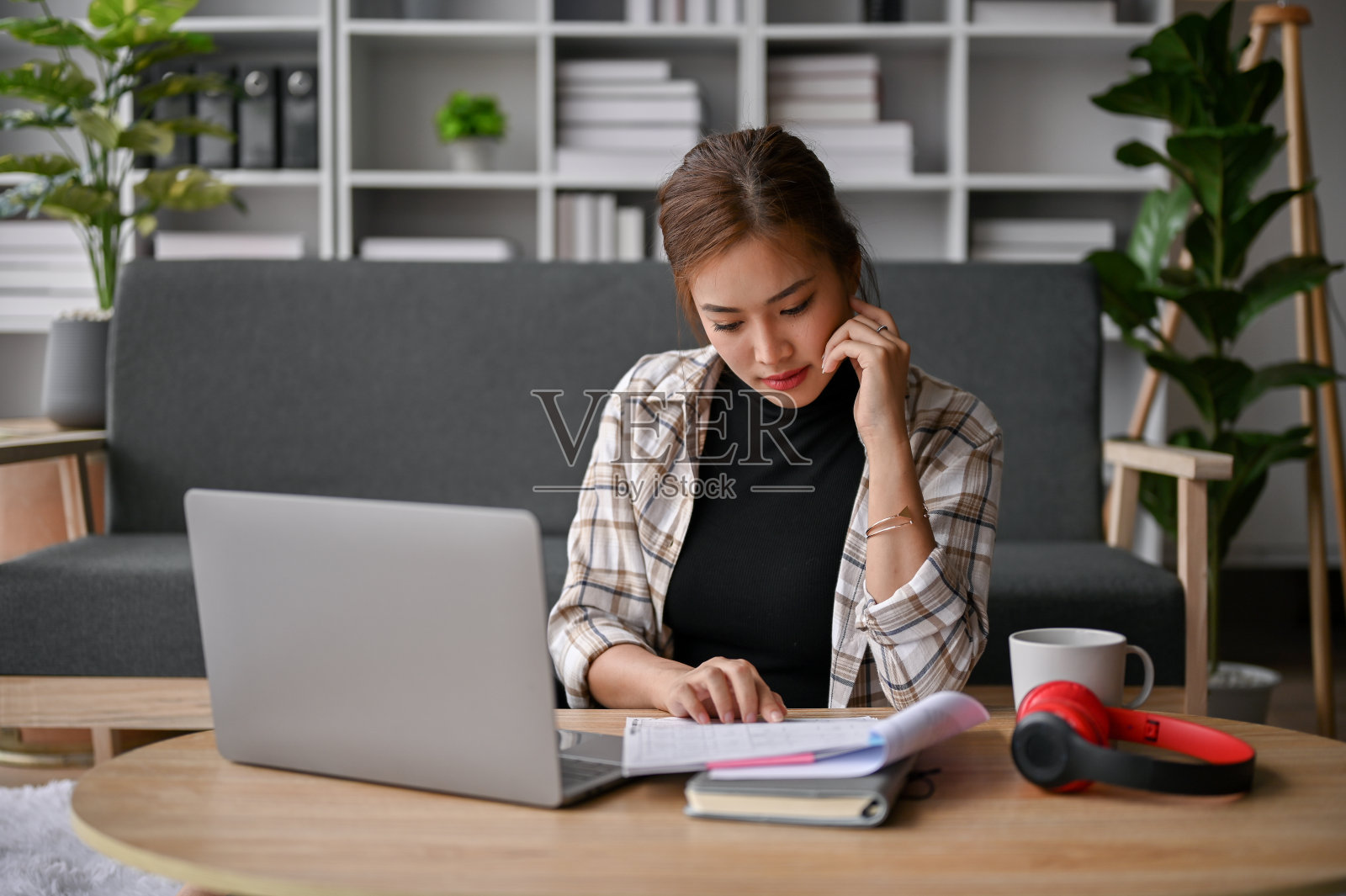 专注的年轻亚洲女性自由职业者在客厅里阅读文件。照片摄影图片