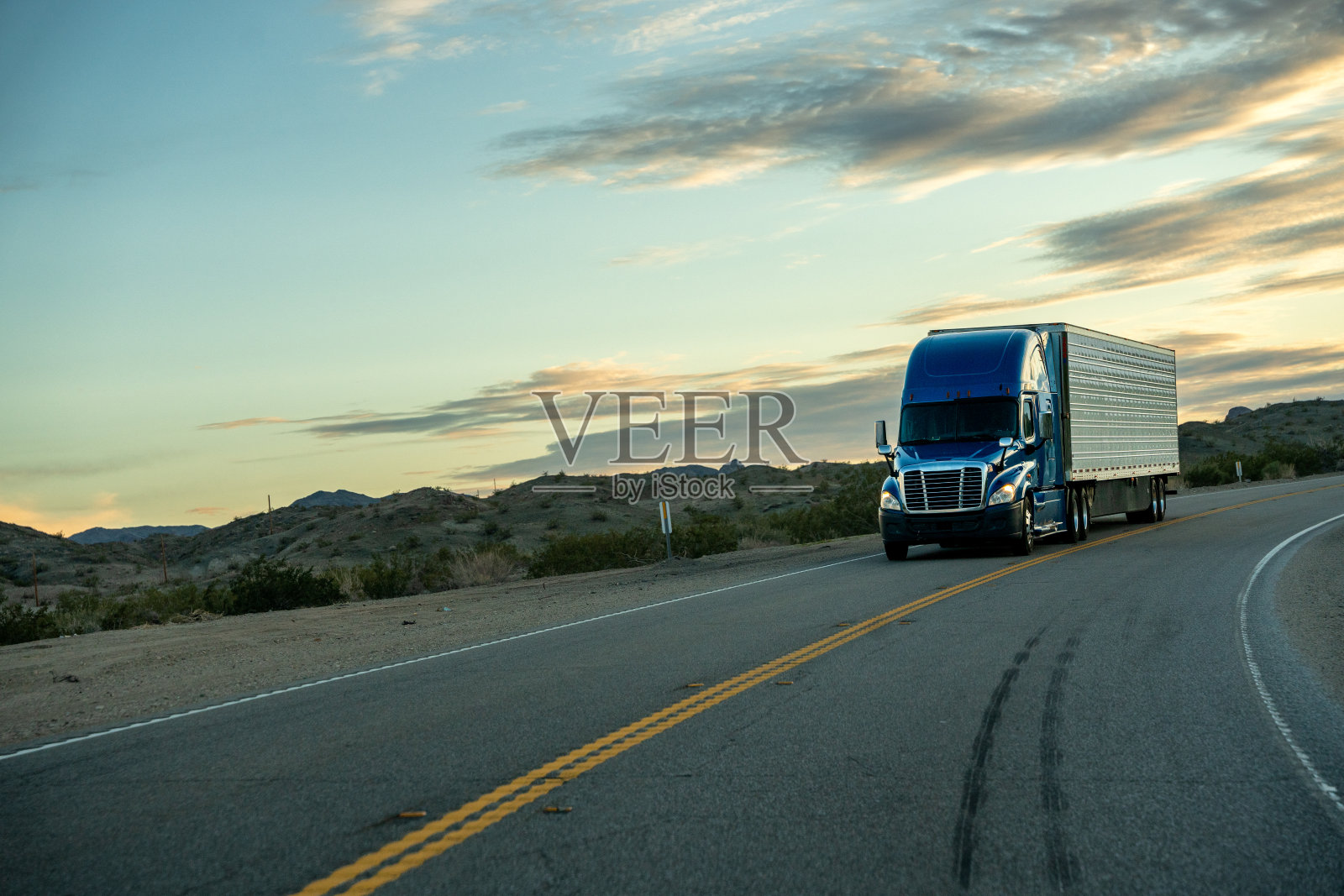 一辆半挂车行驶在两车道的公路上，夕阳下有美丽的云彩照片摄影图片