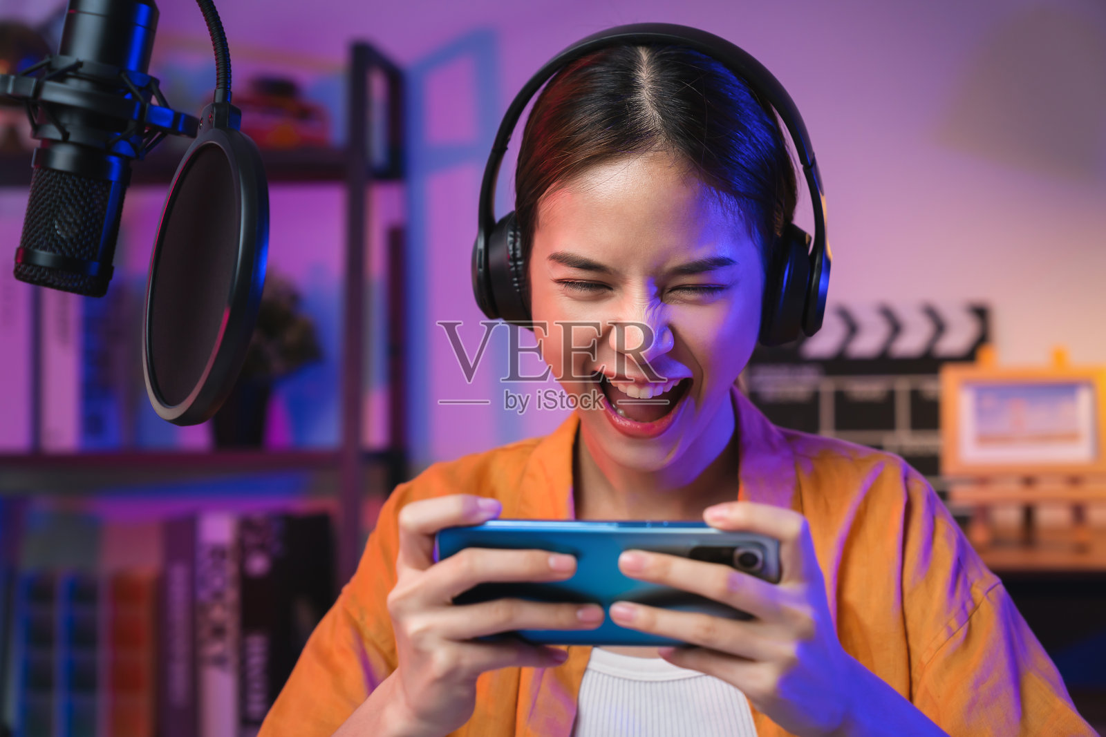 兴奋的年轻亚洲女子戴着耳机，在智能手机上玩在线游戏，在互联网上直播。照片摄影图片