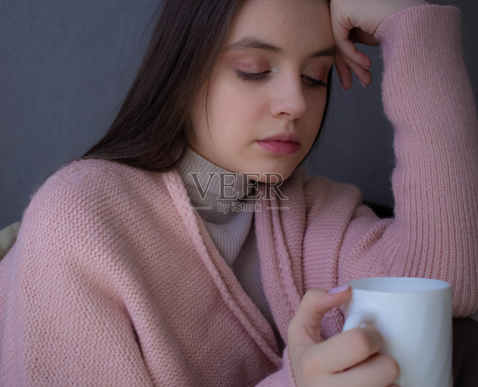 一个生病的女孩坐在温暖的毯子里，端着一杯热茶照片摄影图片