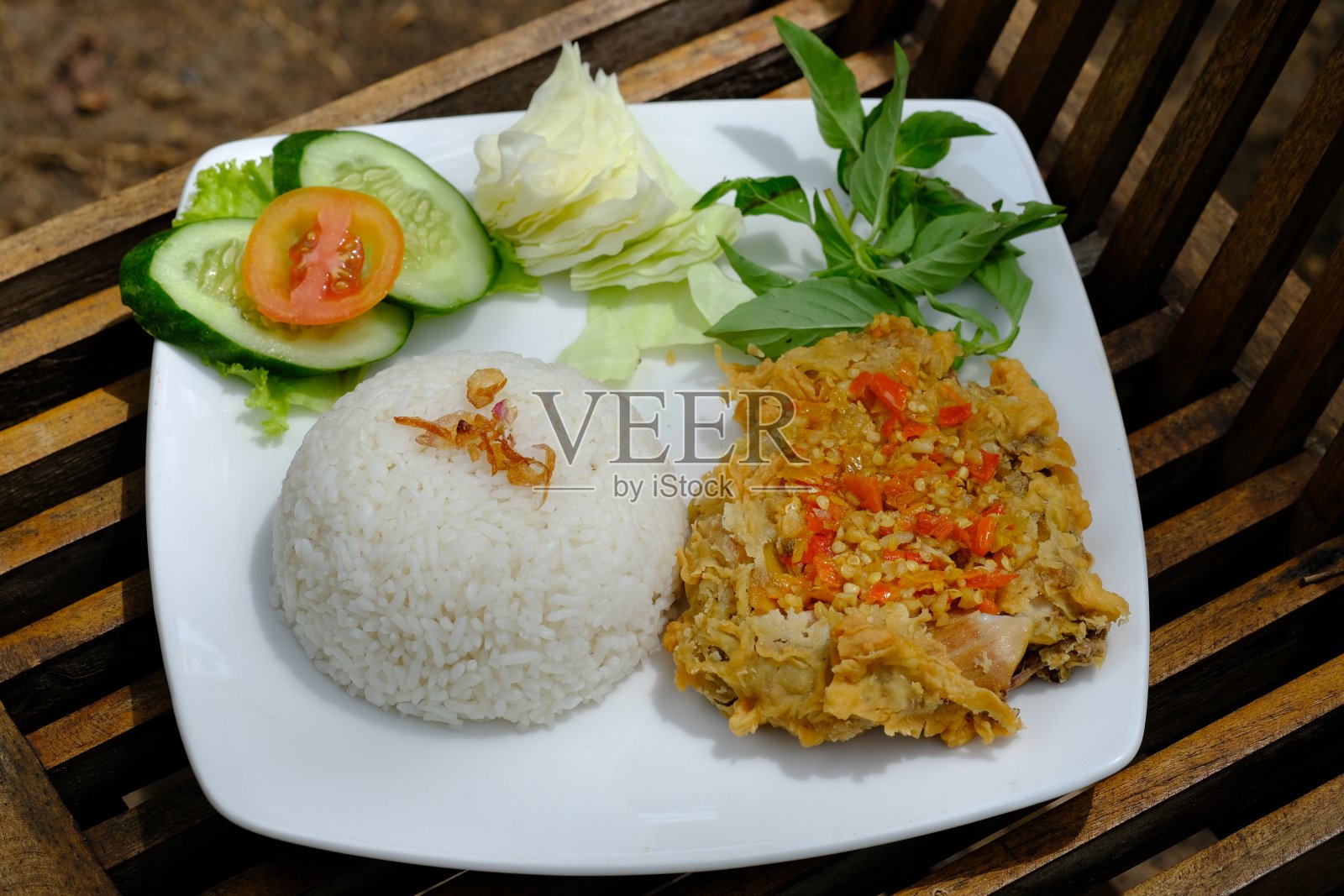 Ayam Geprek，用生辣椒混合辣酱的炸鸡。Ayam sambal pedas。印尼的食物。用白色盘子盛在质朴的棕色桌子上。照片摄影图片