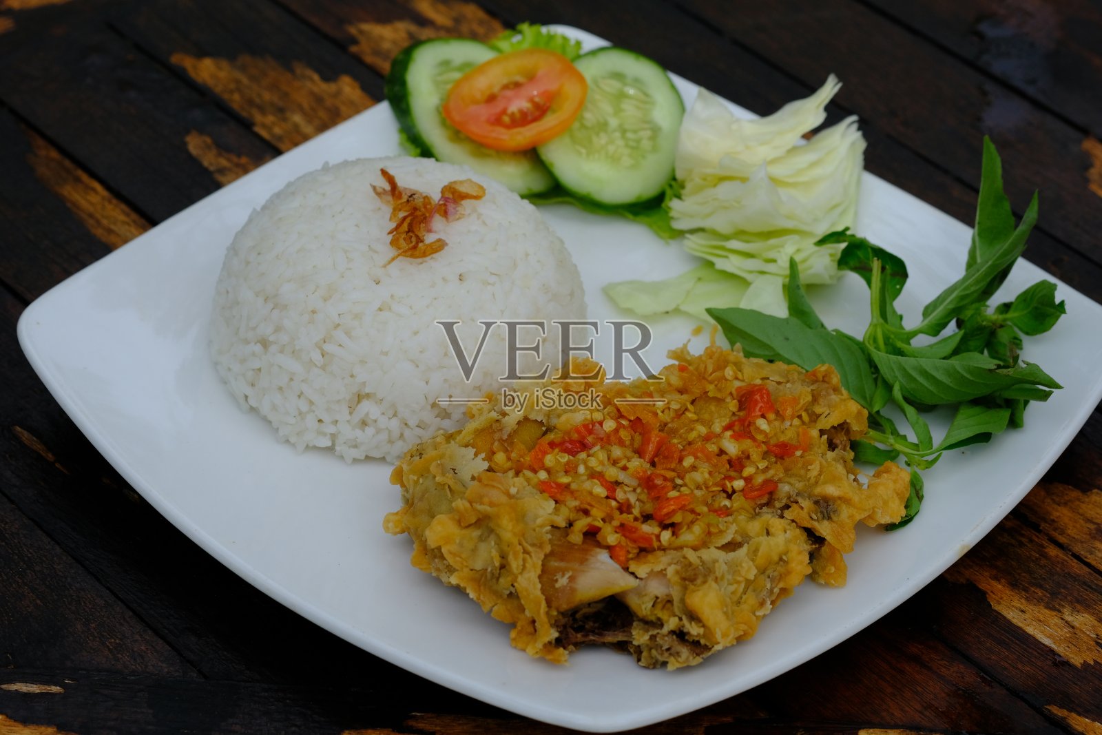 Ayam Geprek，用生辣椒混合辣酱的炸鸡。Ayam sambal pedas。印尼的食物。用白色盘子盛在质朴的棕色桌子上。照片摄影图片