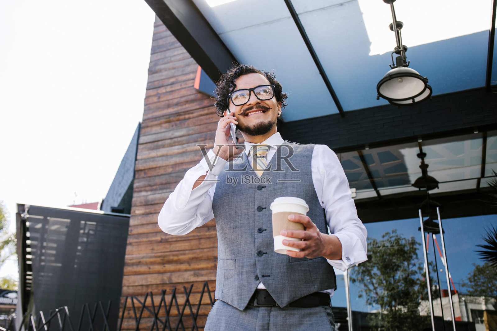 年轻的拉丁商人拿着咖啡杯在墨西哥城的大街上讲手机，西班牙人照片摄影图片
