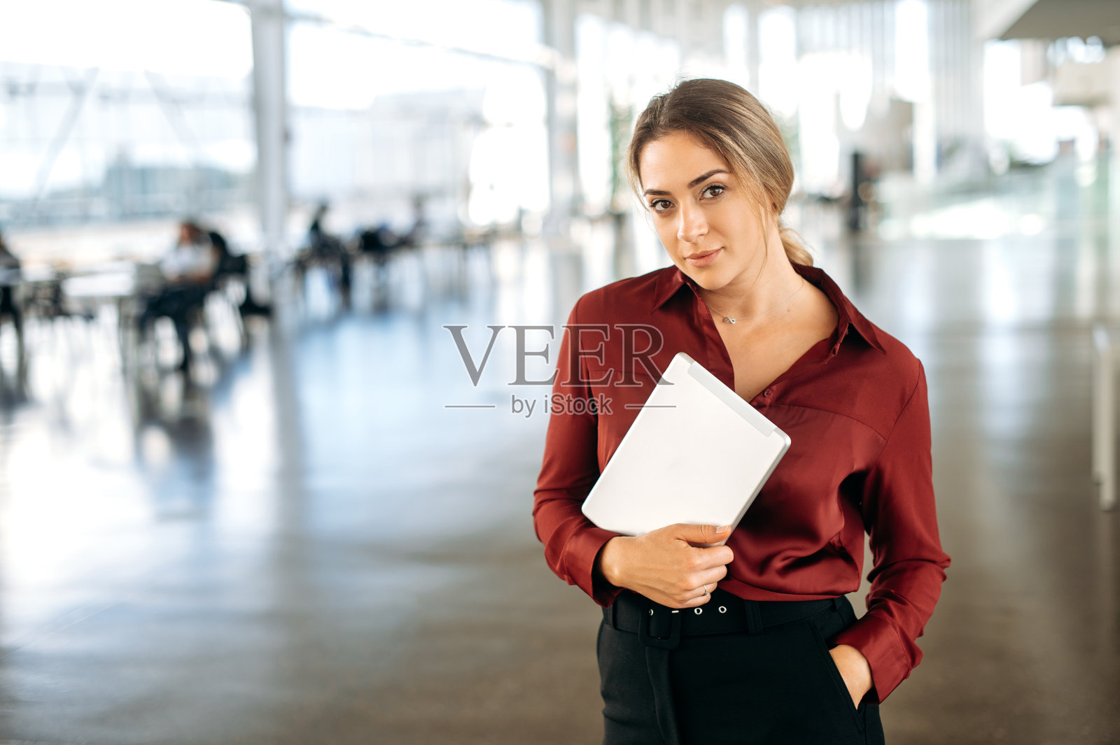 一个积极、优雅、美丽、自信、成功的金发白人商务女性的肖像，穿着衬衫，站在联合办公中心，手里拿着平板电脑，看着镜头照片摄影图片