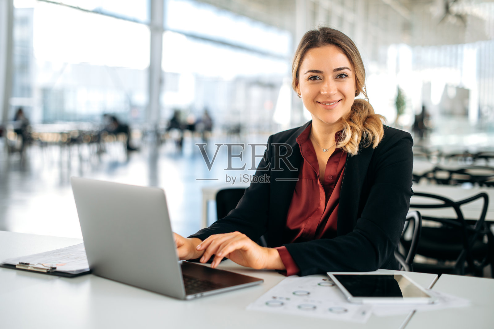 成功自信的白人商务女性，穿着优雅，高管，招聘，产品经理，坐在现代化的办公室里，用笔记本电脑工作，看着相机，友好地微笑照片摄影图片
