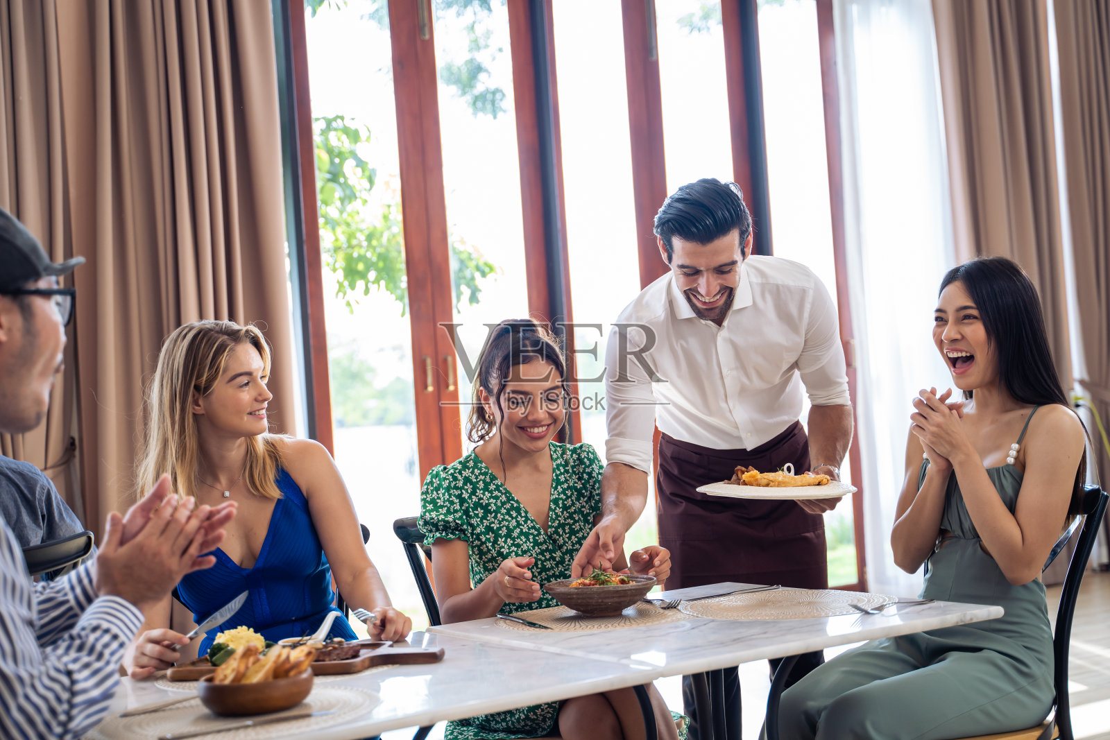 一群不同的朋友在餐厅里聊天、吃饭。有魅力的年轻男女让人们感到快乐和放松，在室内玩乐，在咖啡馆聚会和团聚。照片摄影图片