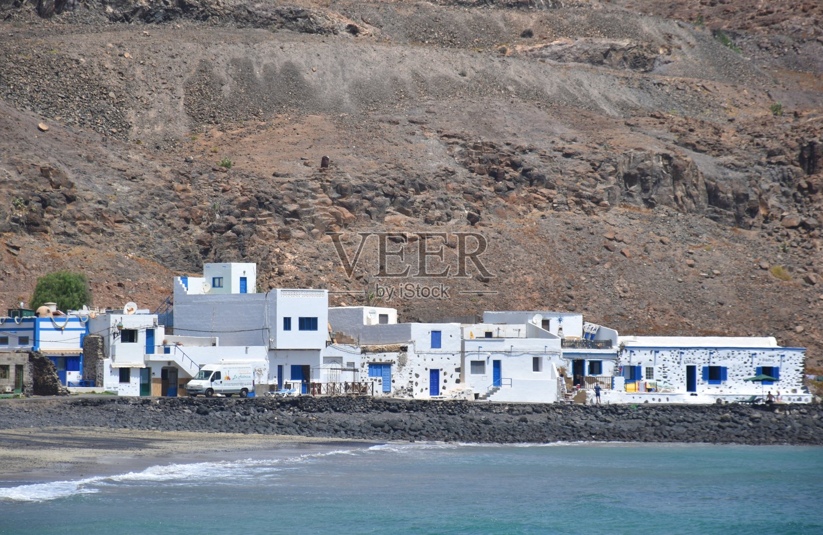 西班牙加那利群岛富埃特文图拉岛，波佐内格罗海滩悬崖前的田园诗般的村庄，白色的房子照片摄影图片