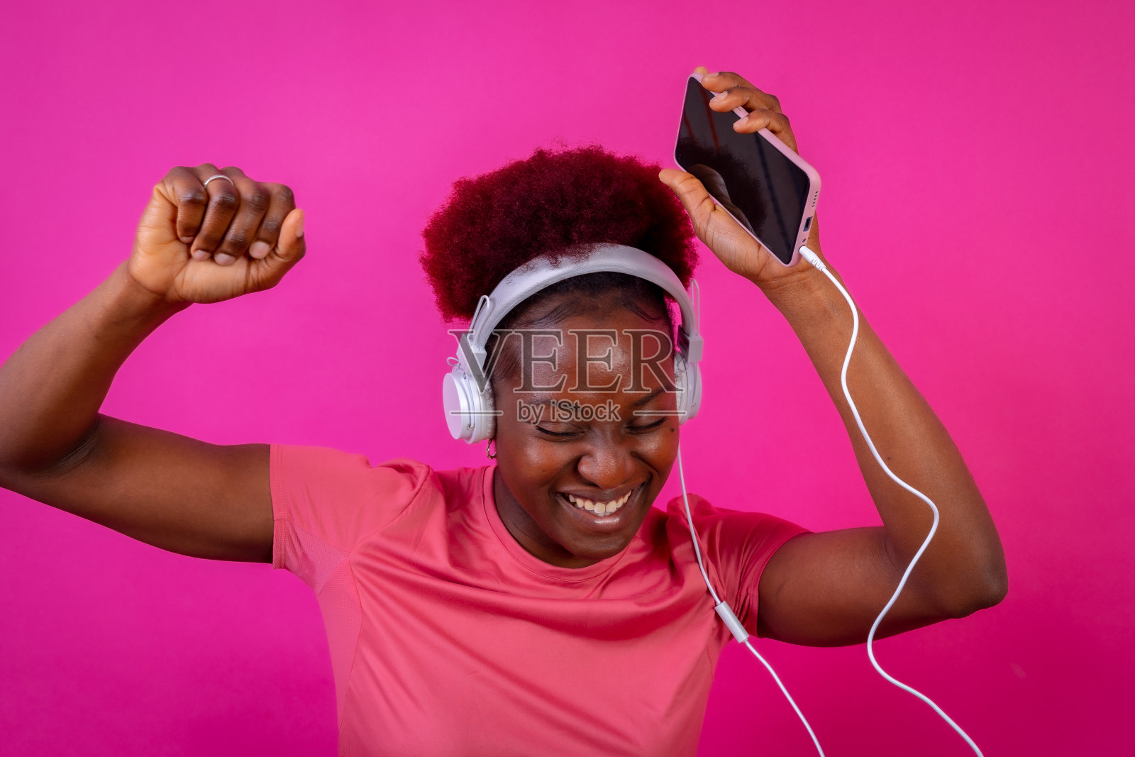 年轻的非裔美国妇女孤立在粉红色的背景与耳机跳舞，工作室拍摄照片摄影图片