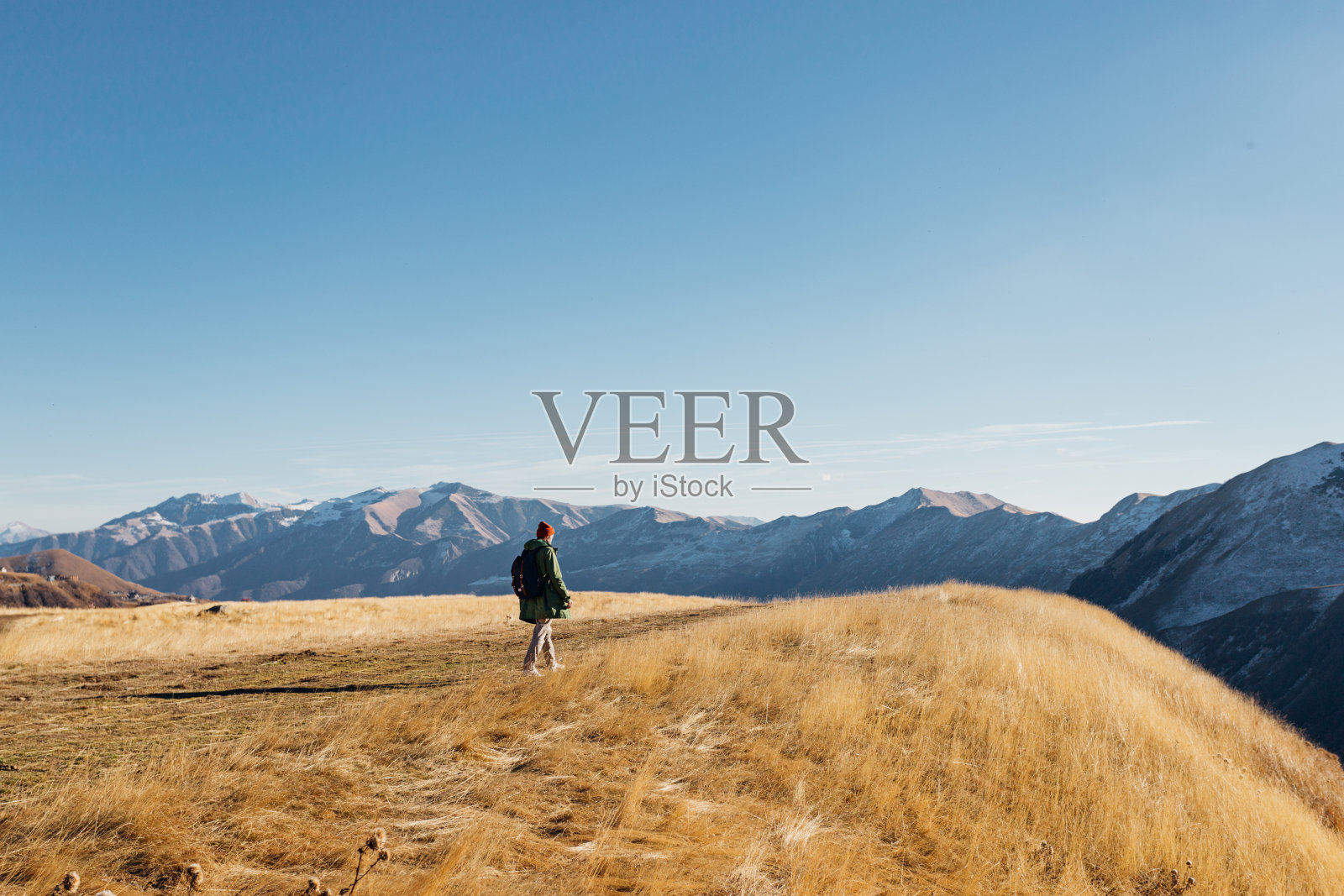 秋天，一个男人在雪峰山的山坡或悬崖上走过一片枯黄的草地照片摄影图片