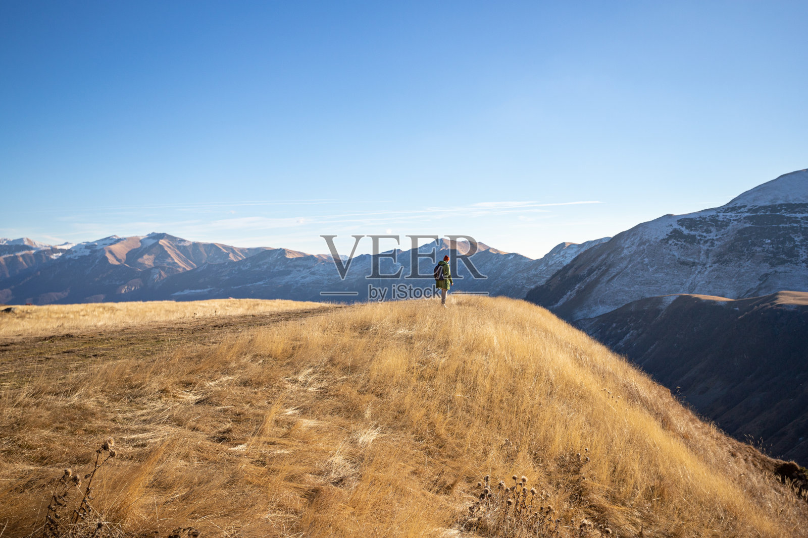 秋天，一个人站在白雪皑皑的山峰上，枯黄的草地上的斜坡或悬崖上照片摄影图片